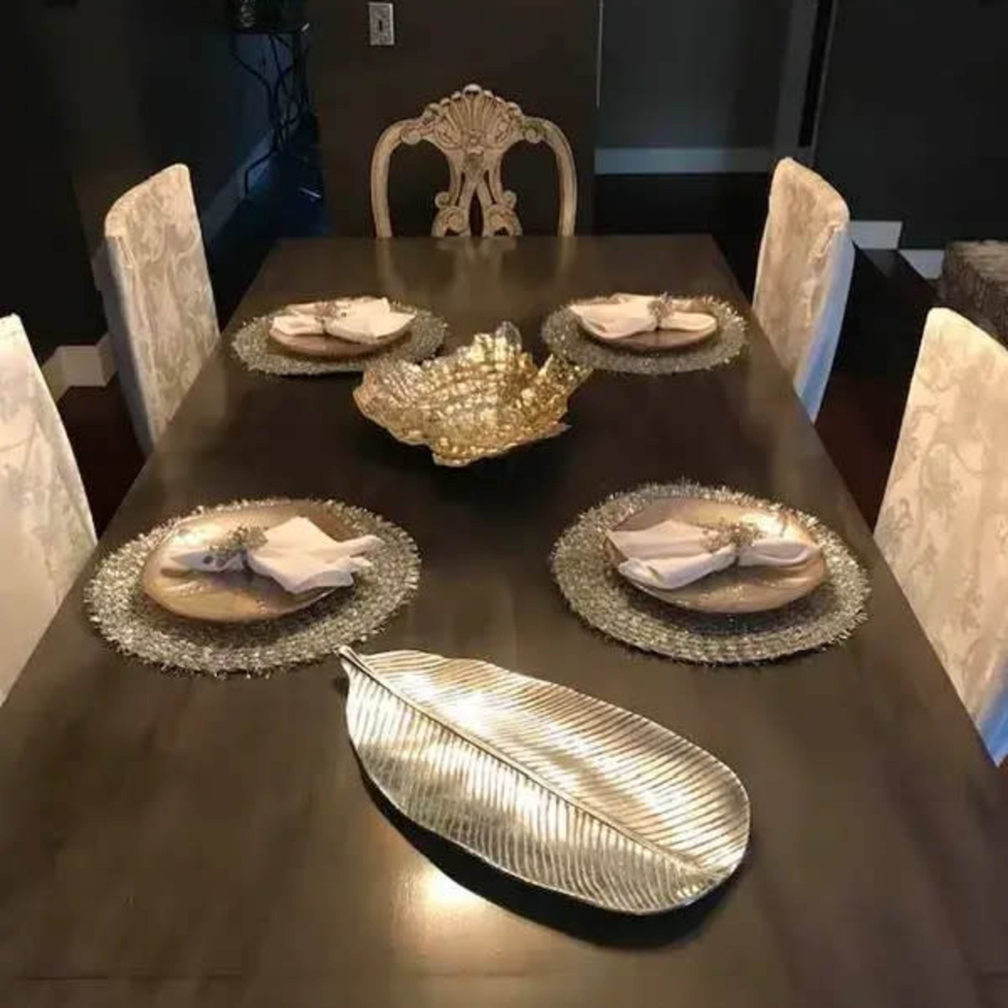A dining table is set with decorative plates and napkins, positioned around a central ornamental bowl and a leaf-shaped dish.