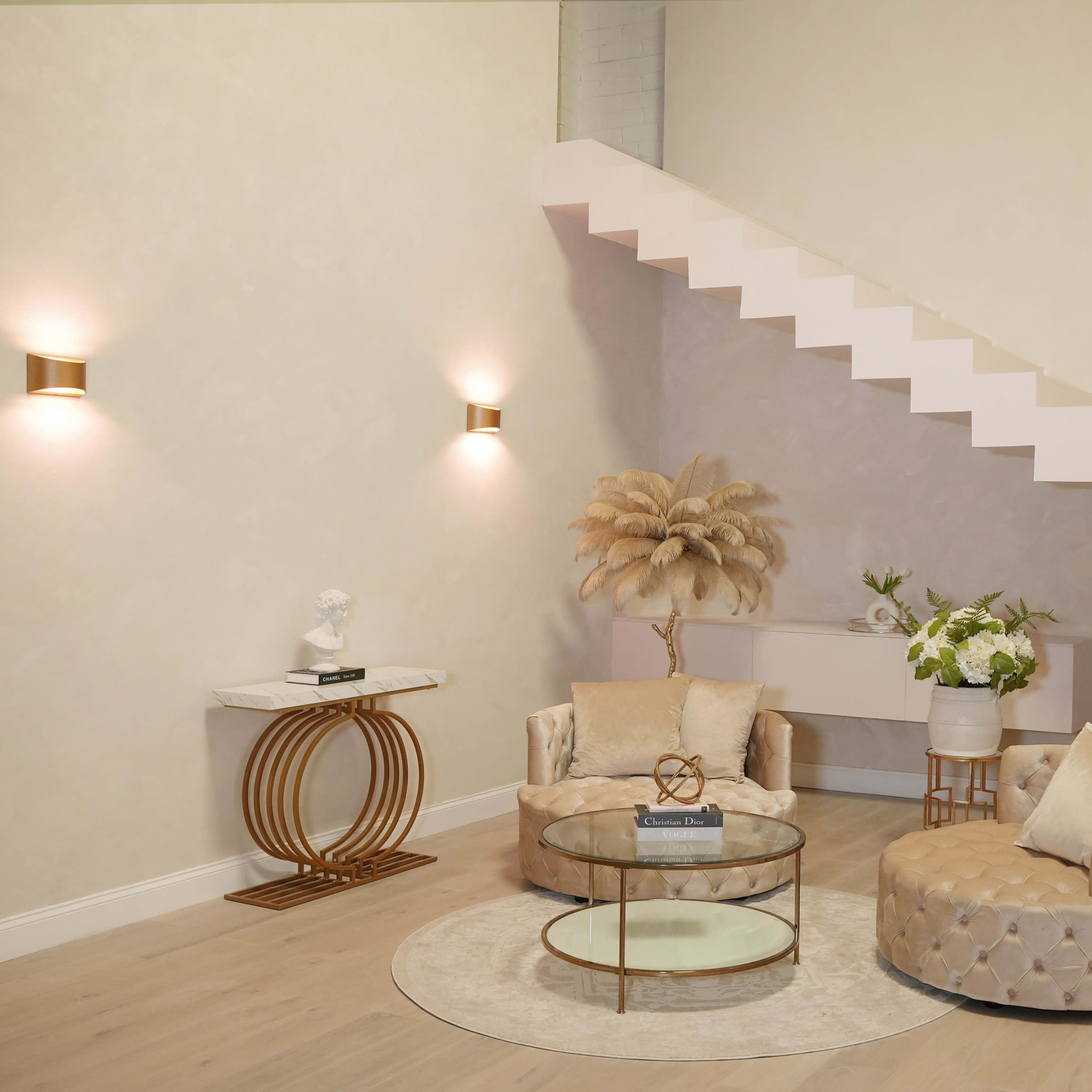 A modern living space with two plush armchairs, a round glass coffee table, and a staircase with minimalist design elements.