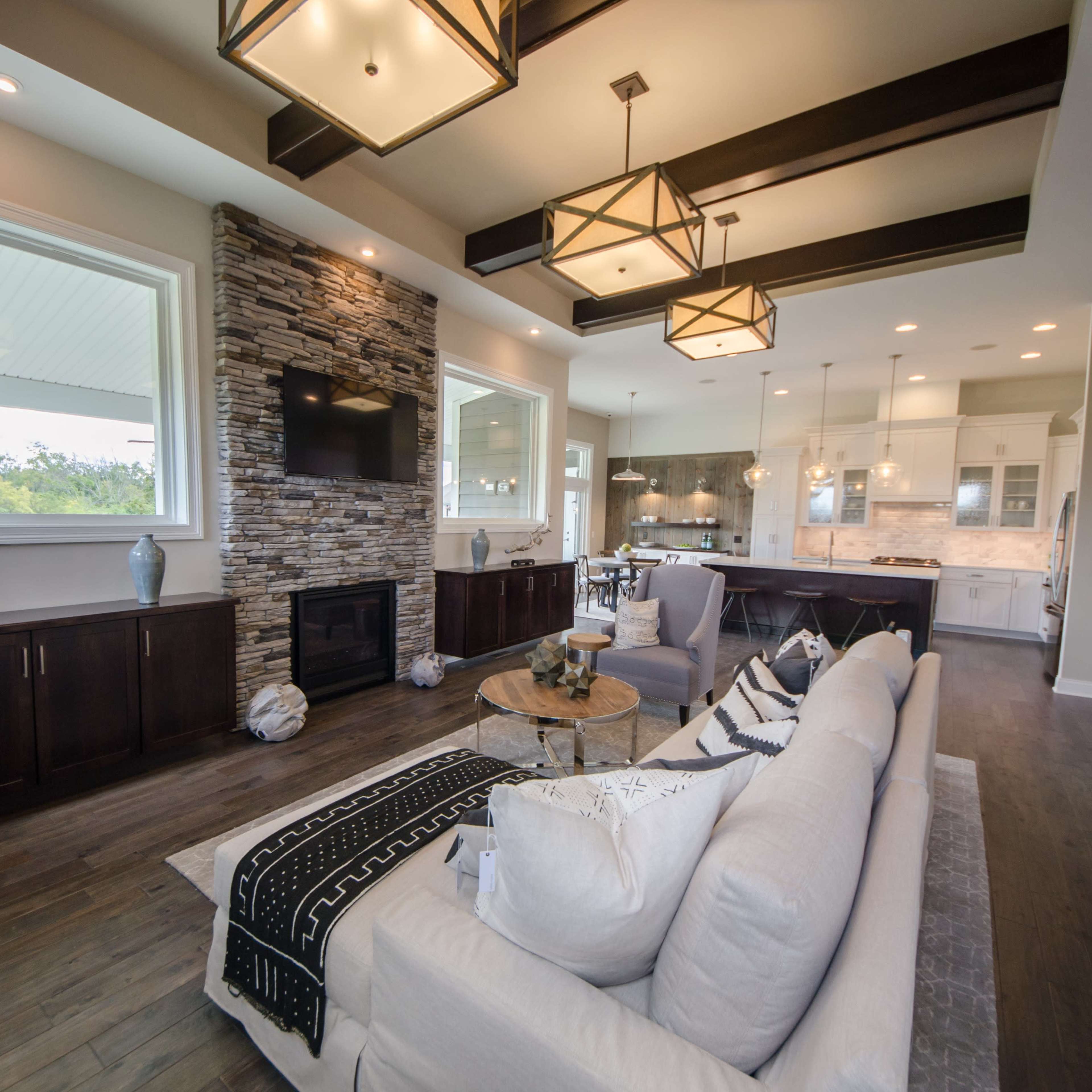 A modern living room with wooden floors, a stone fireplace, large windows, and a sectional sofa.