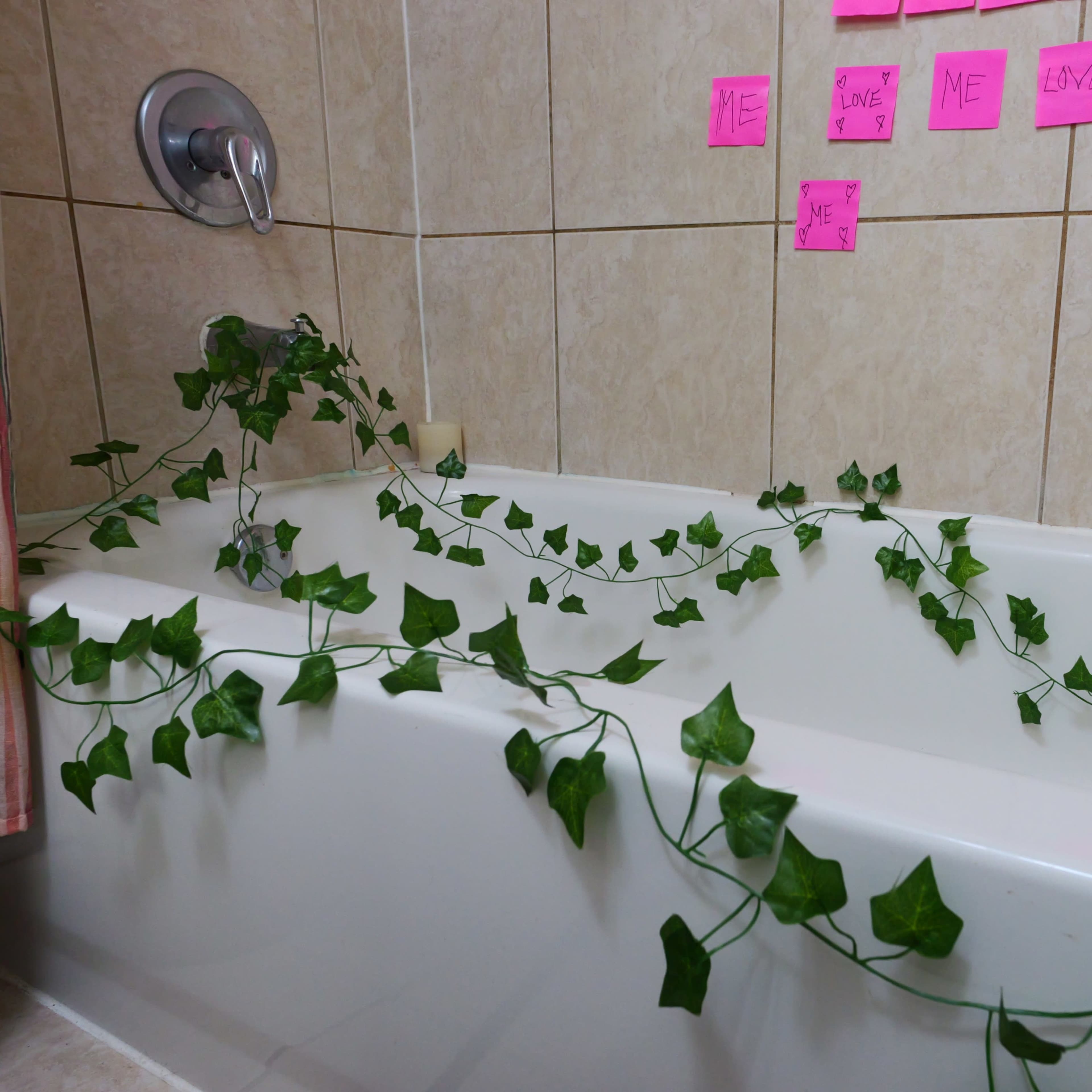 A bathtub is surrounded by a long vine of green leaves and bright pink sticky notes on the wall.