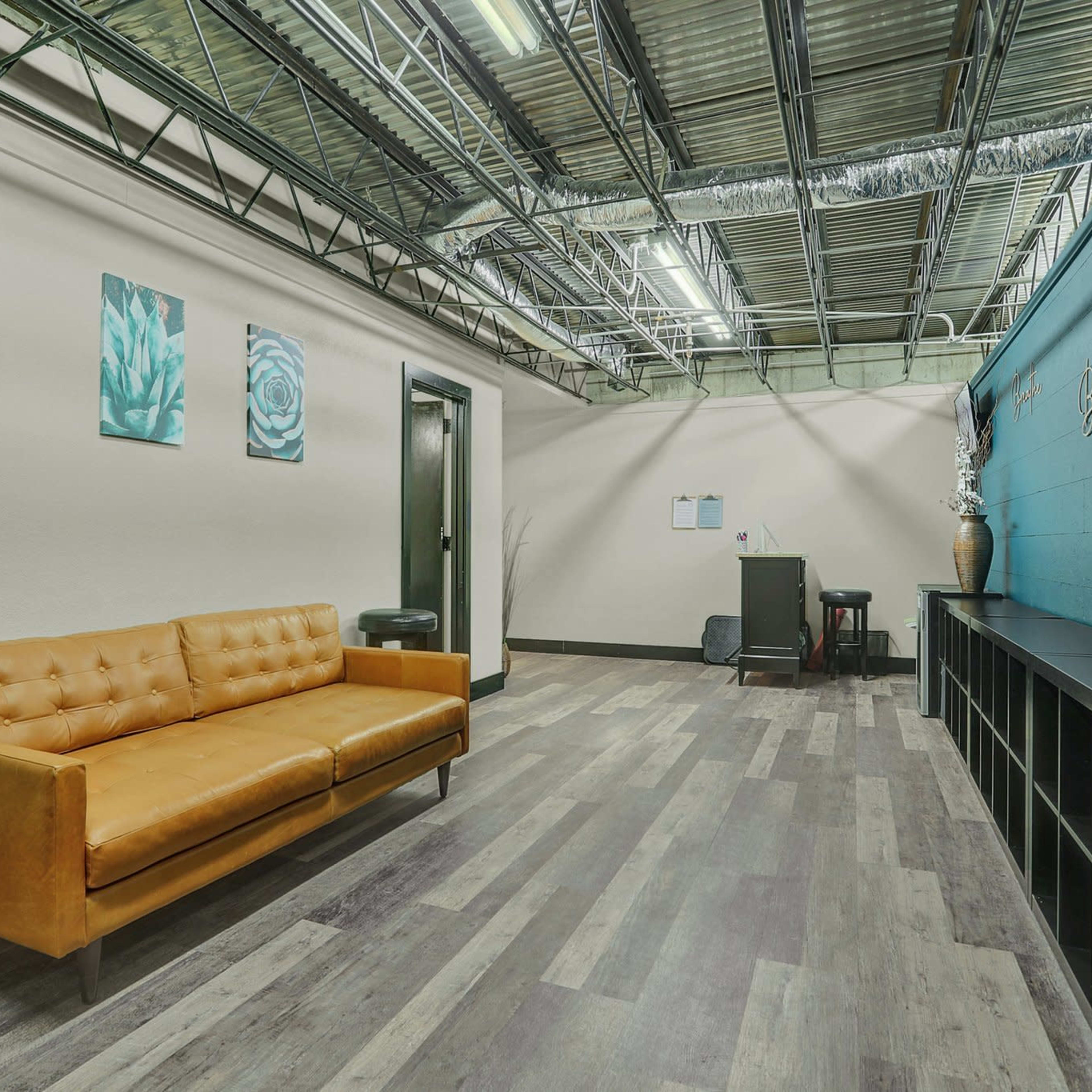 A modern office space with a brown leather sofa, teal wall art, and a desk against a blue accent wall.