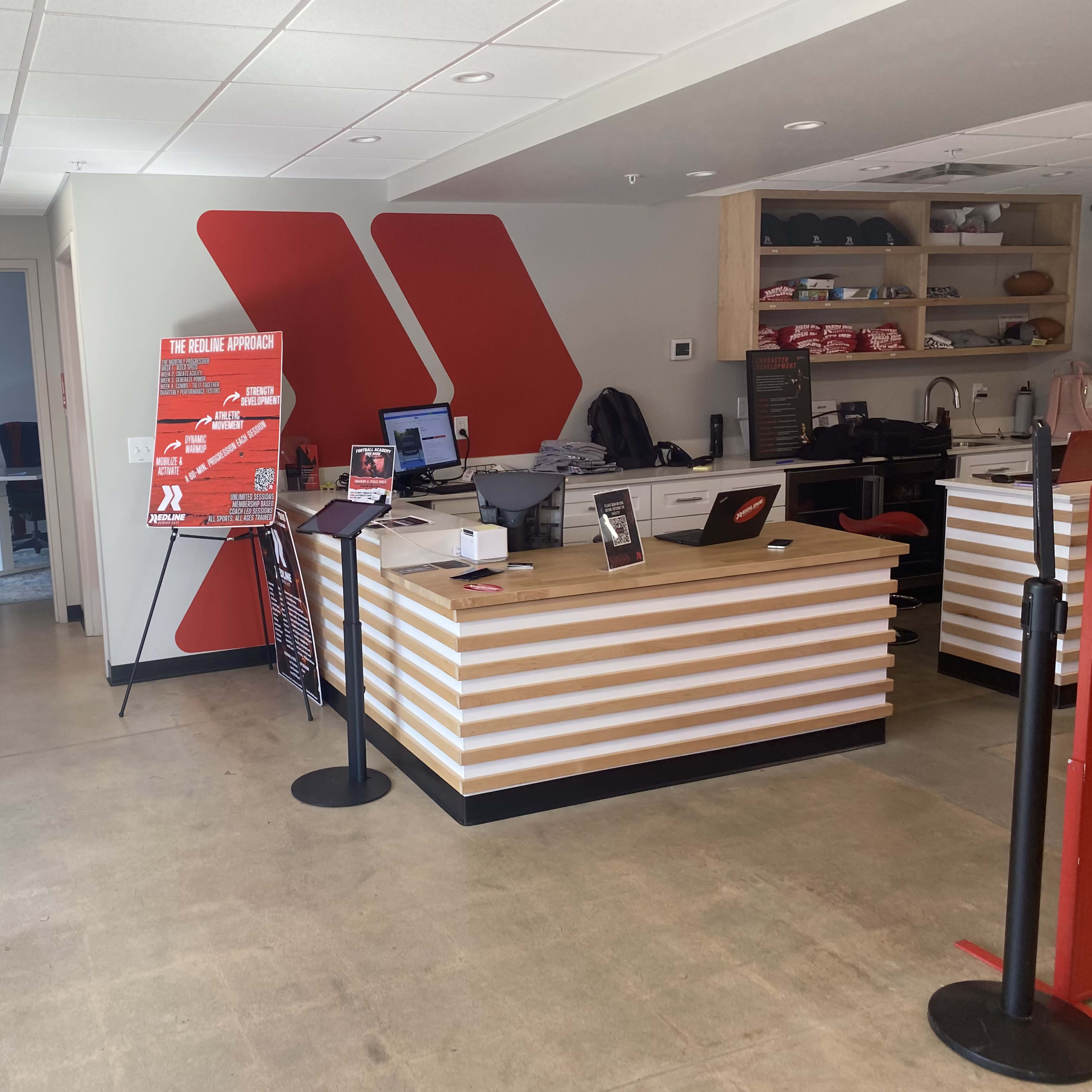 A modern reception area with a striped wooden front desk, red accent walls, and a display stand featuring promotional materials.