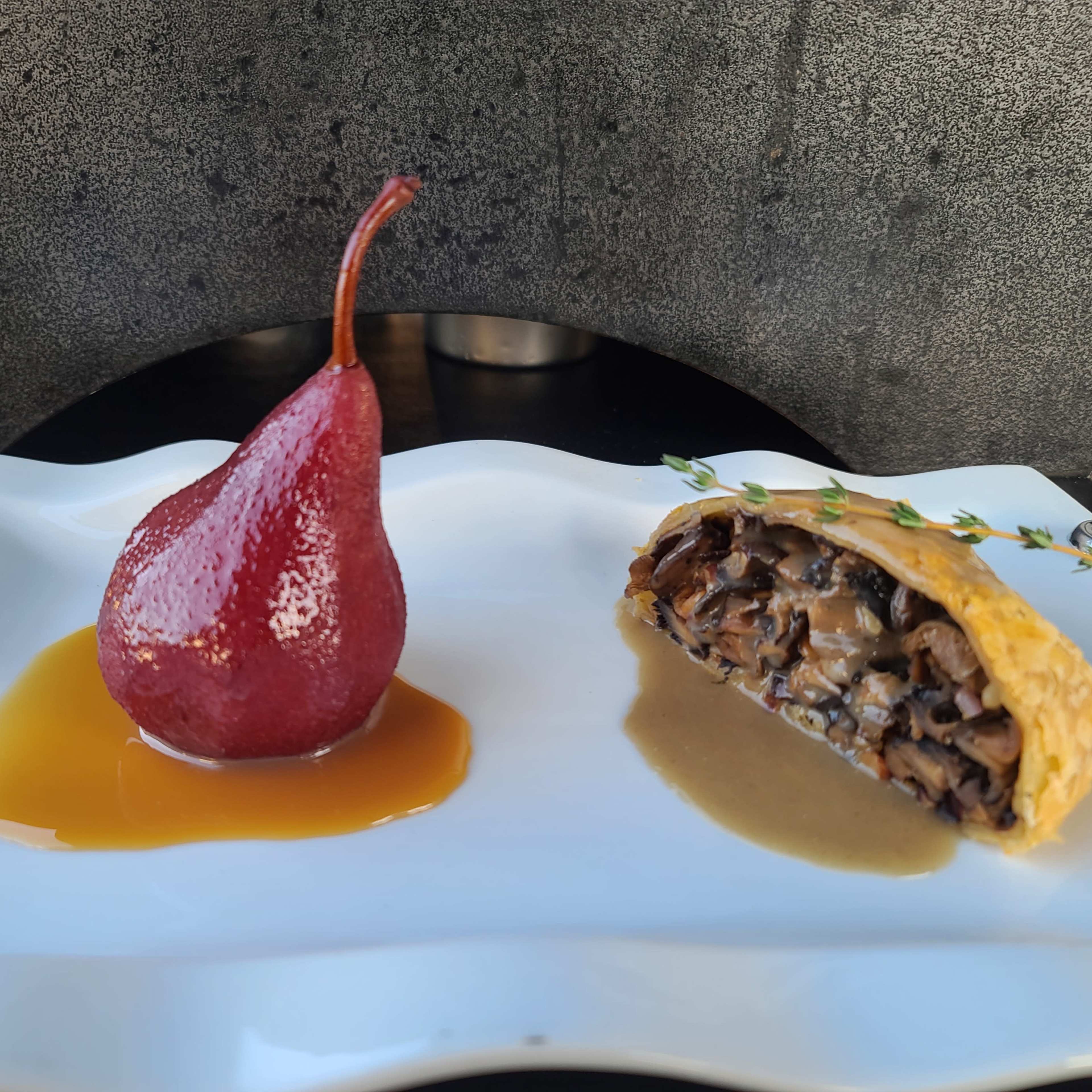 The dish features a glossy red pear alongside a slice of pastry filled with mushrooms and served with a creamy sauce.