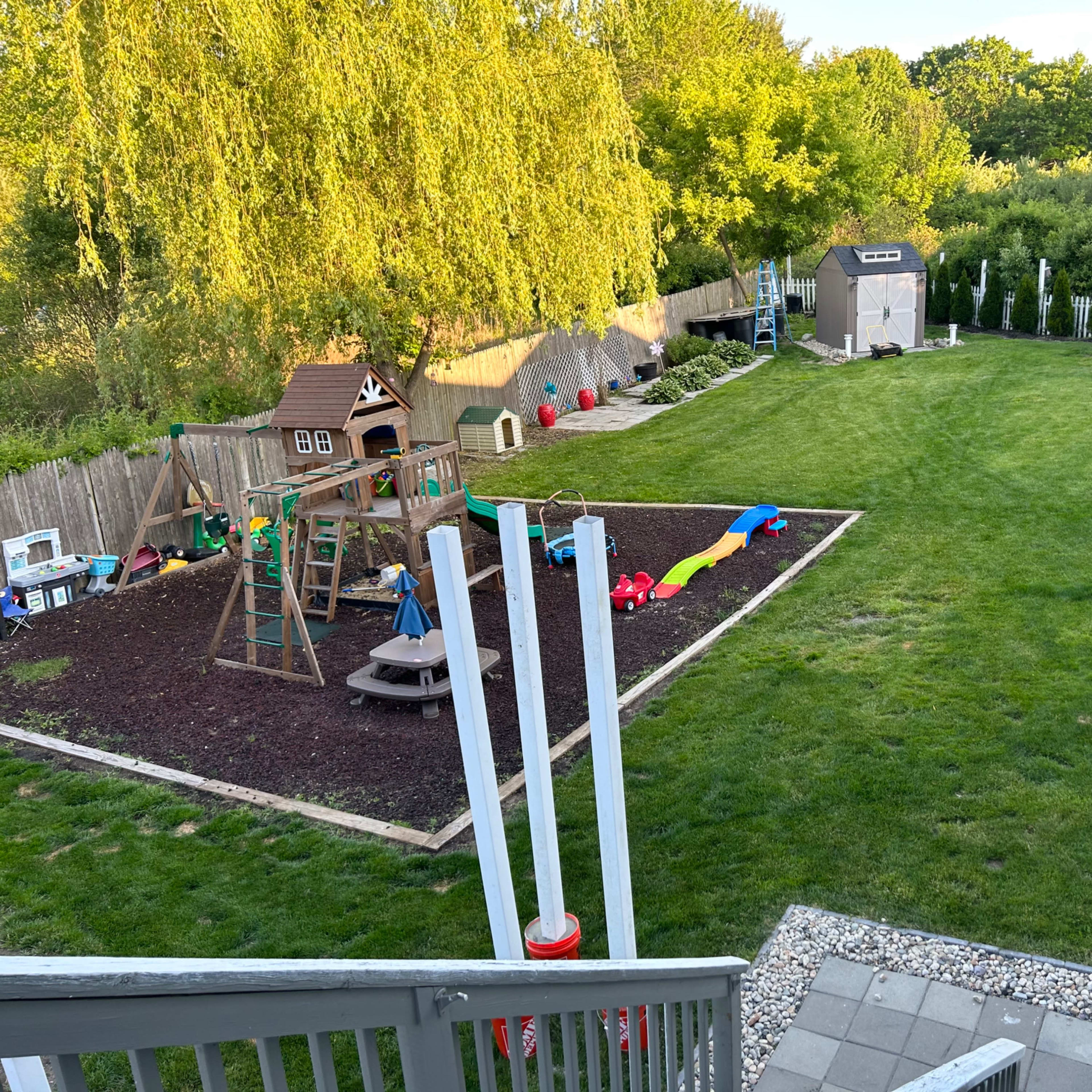 A backyard play area featuring a playground structure, a sandbox, and colorful play equipment set on grass.
