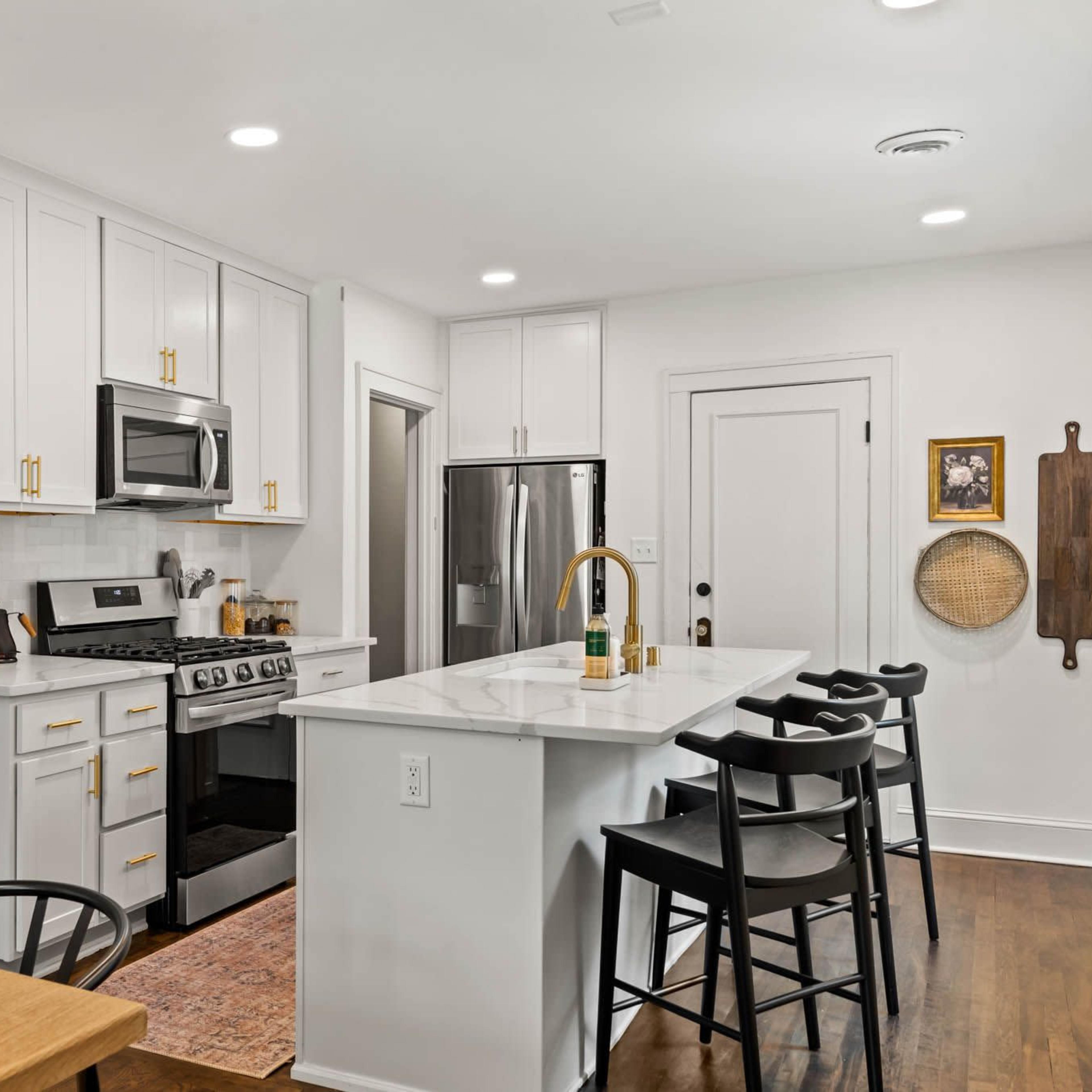 A modern kitchen with white cabinetry, stainless steel appliances, and a central island with bar stools.