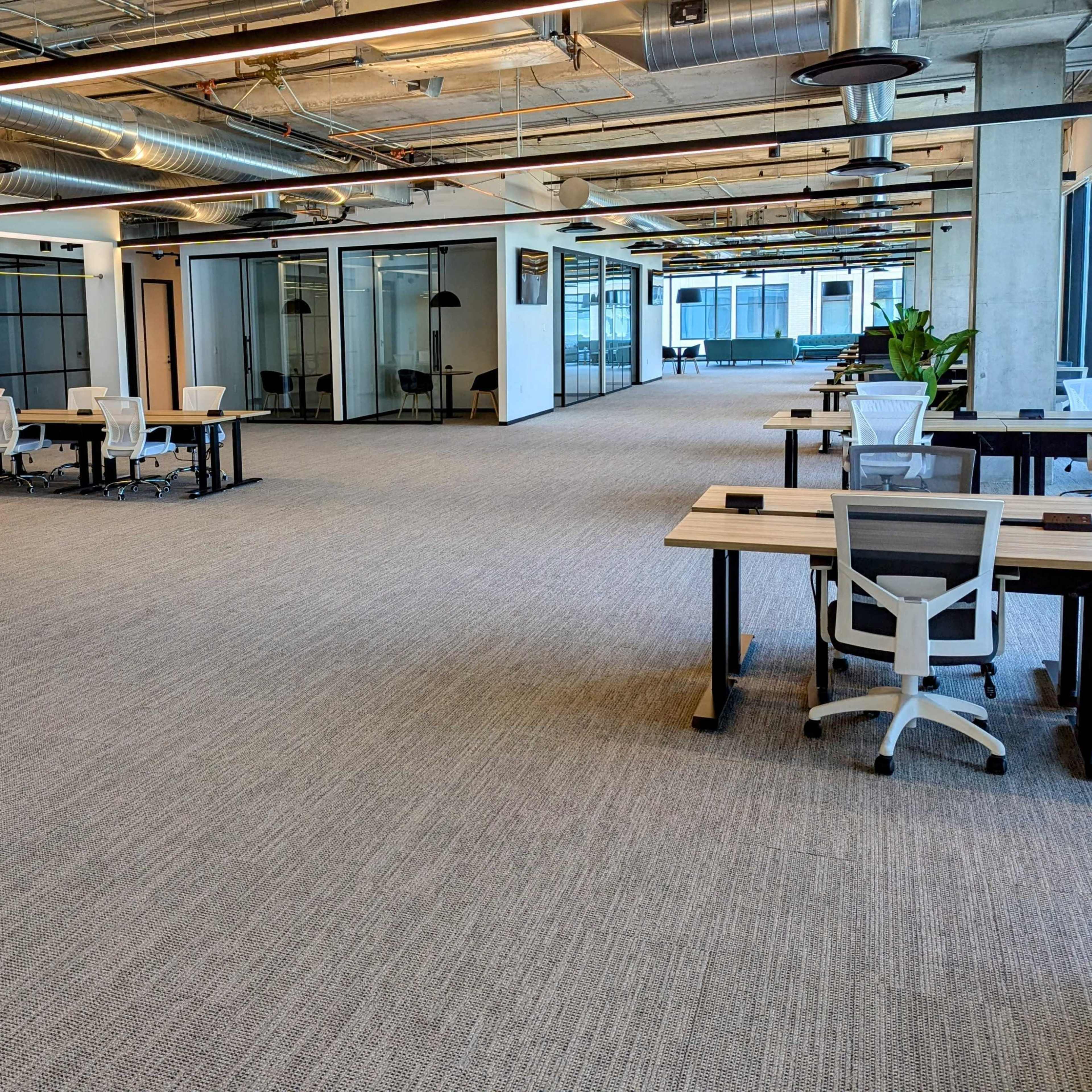 An open office space features rows of desks and chairs with glass-walled meeting rooms in the background.