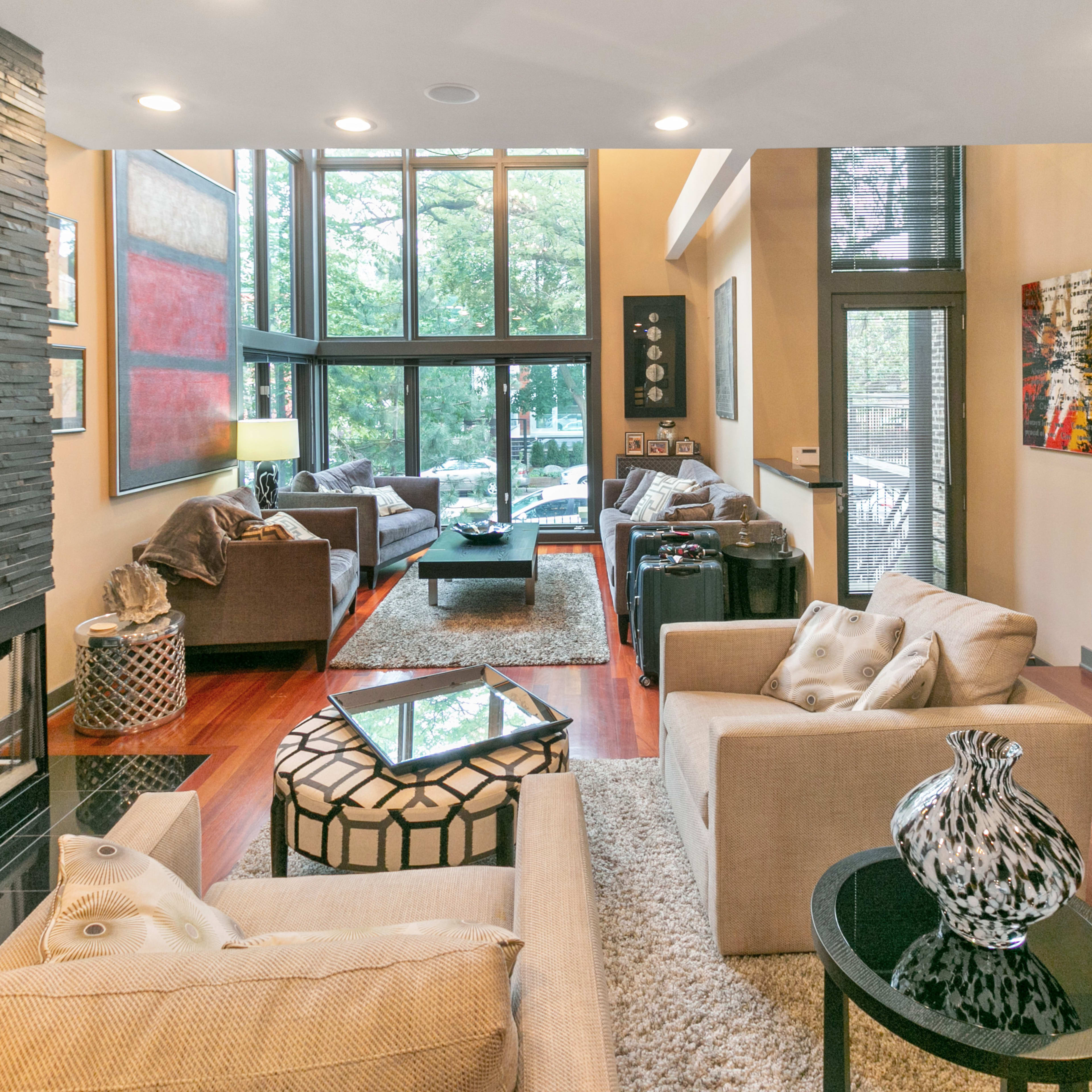 A modern living room features large windows, a stone fireplace, and comfortable seating arrangements with decorative elements.