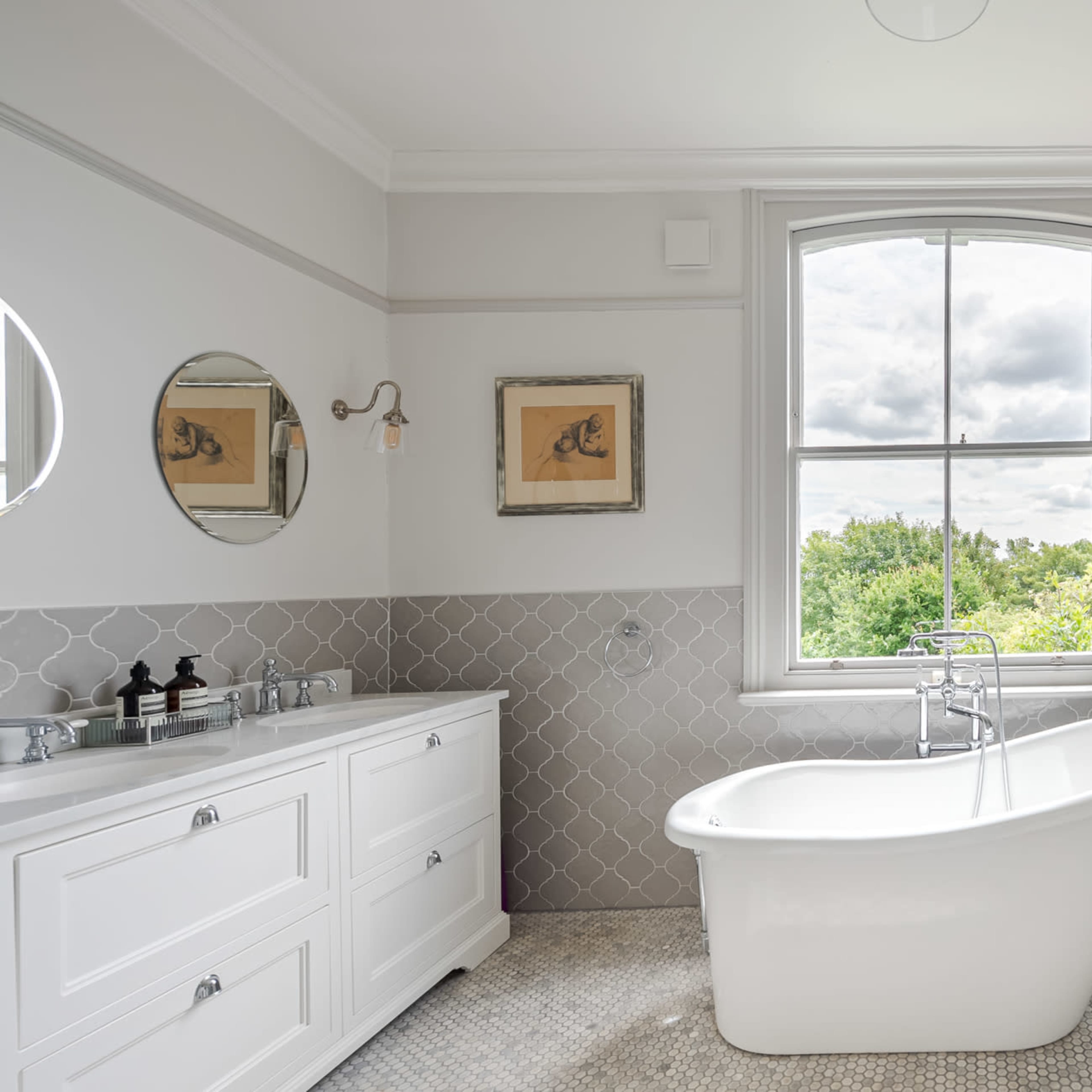 A modern bathroom features a freestanding bathtub, a glass shower enclosure, a dual-sink vanity, and a large window with a view.