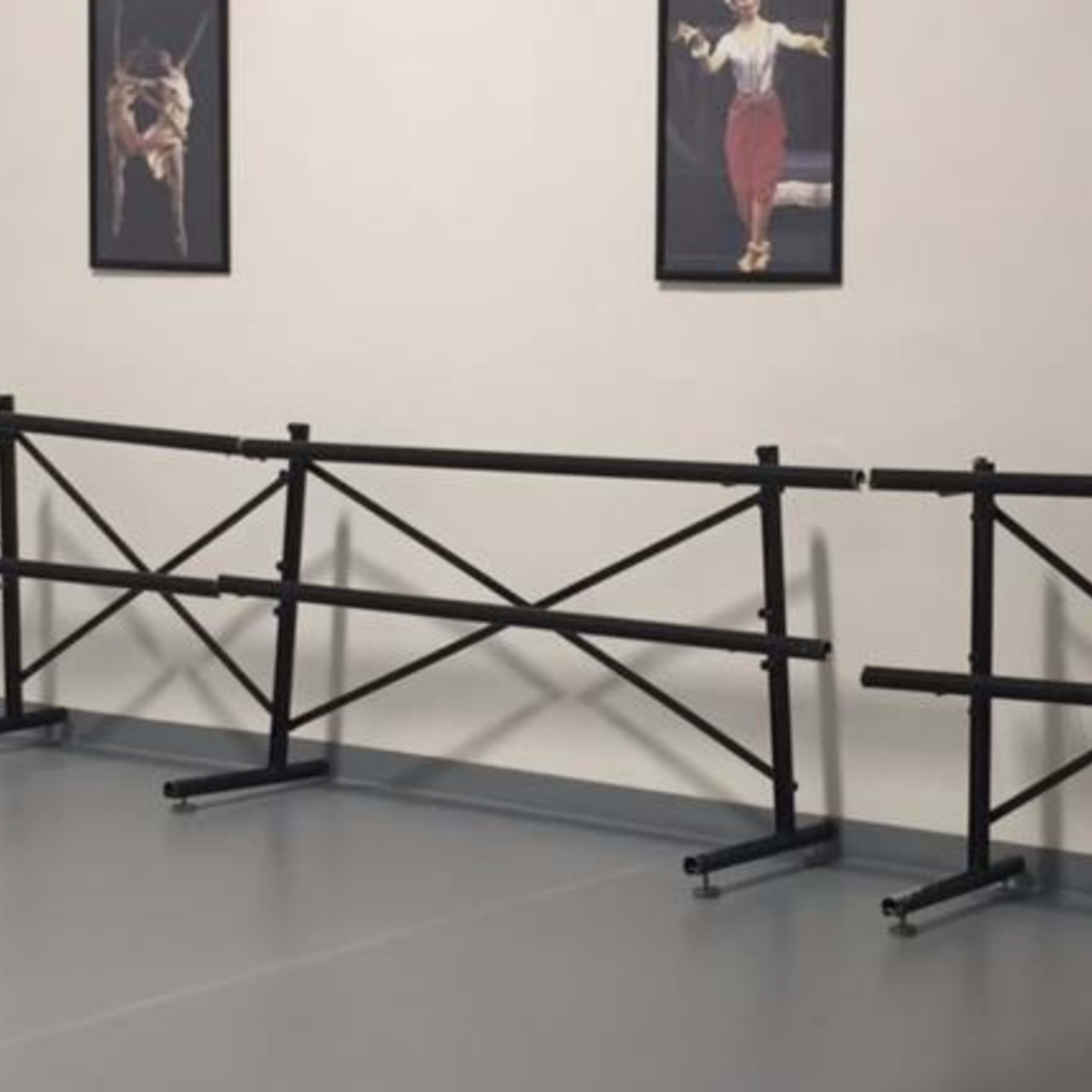 Several black ballet barres positioned in a dance studio with framed dance-related artwork on the wall.