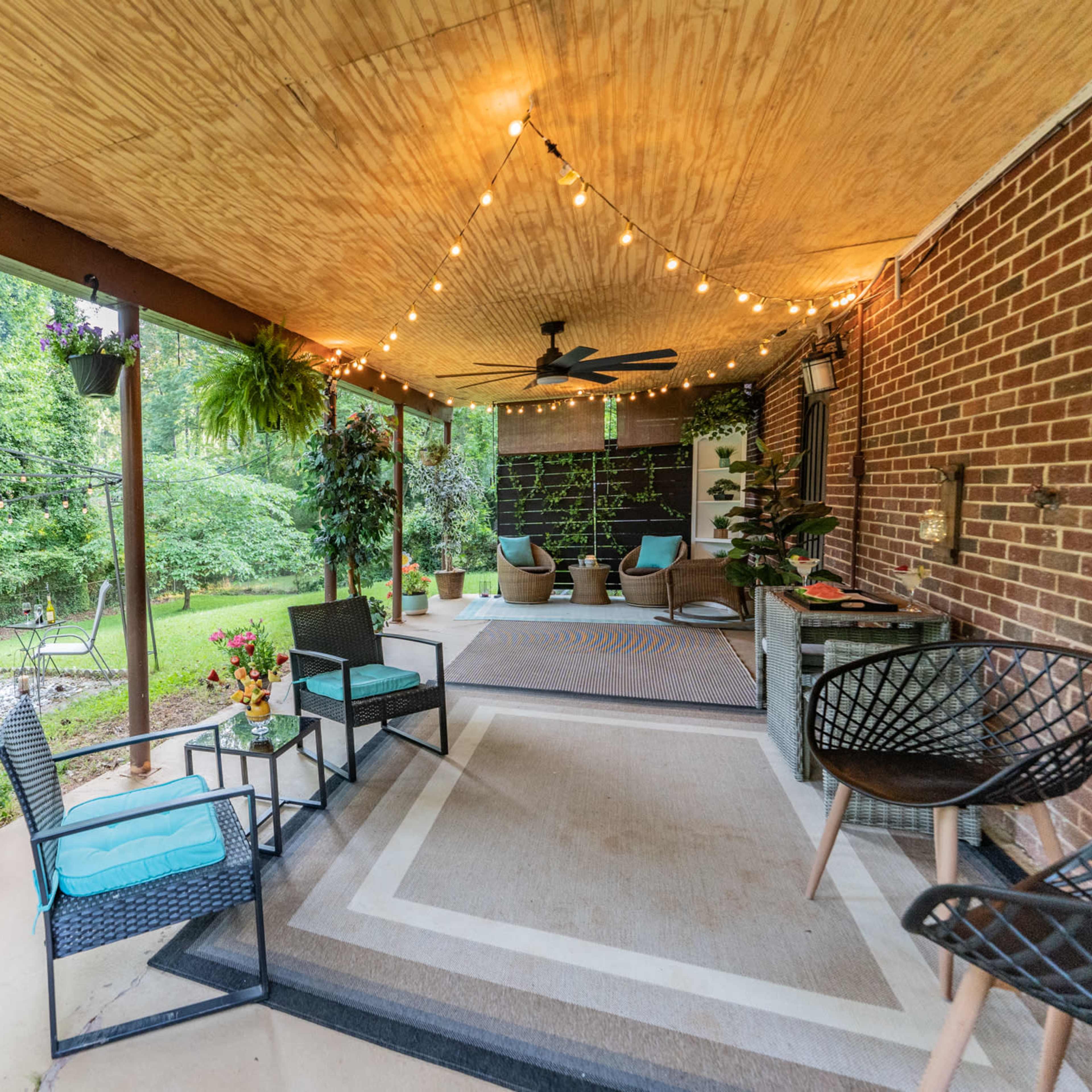 A covered patio with seating, string lights overhead, and a view of a green backyard featuring a fire pit and chairs.
