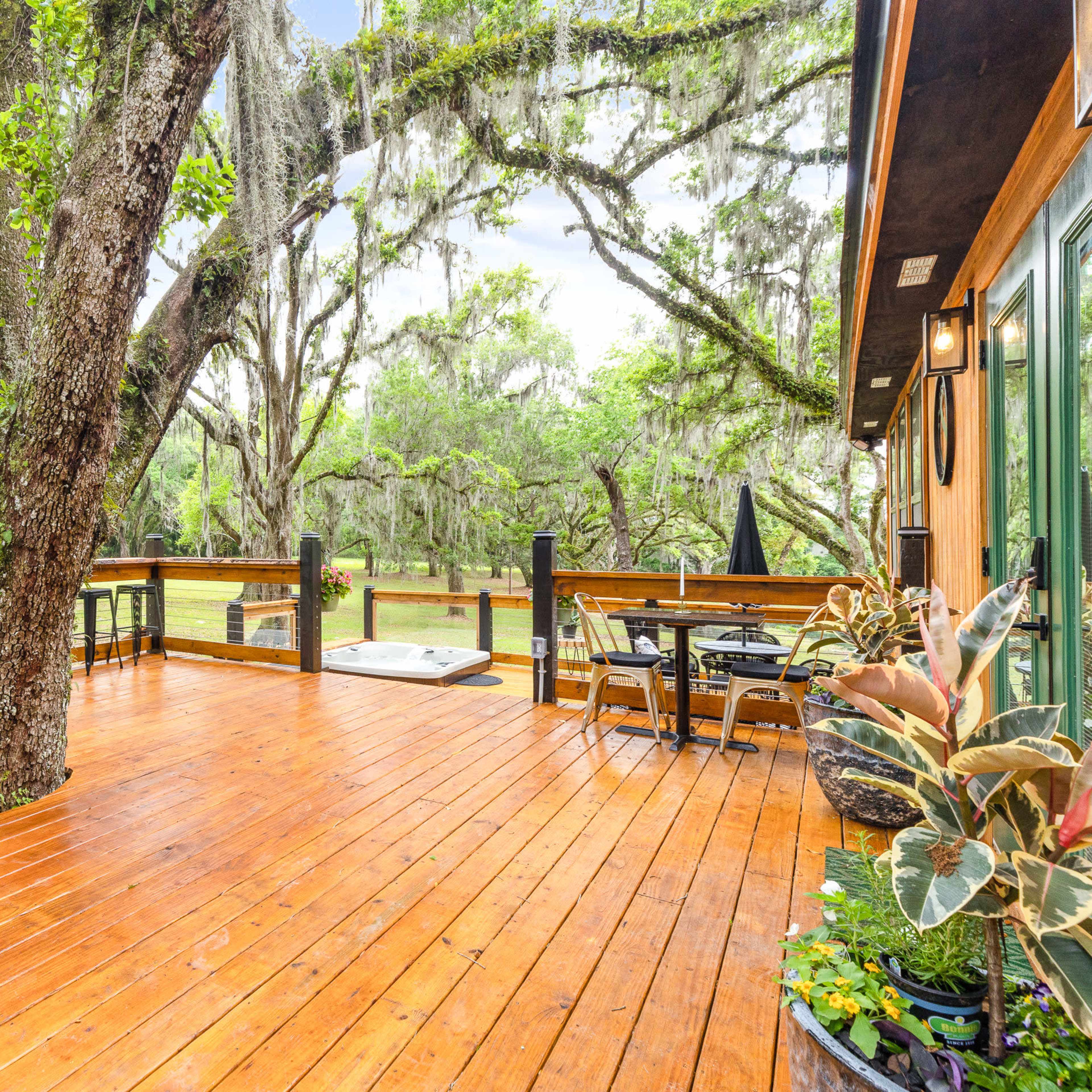 A wooden deck features a large tree at its center, surrounded by outdoor furniture and lush greenery.