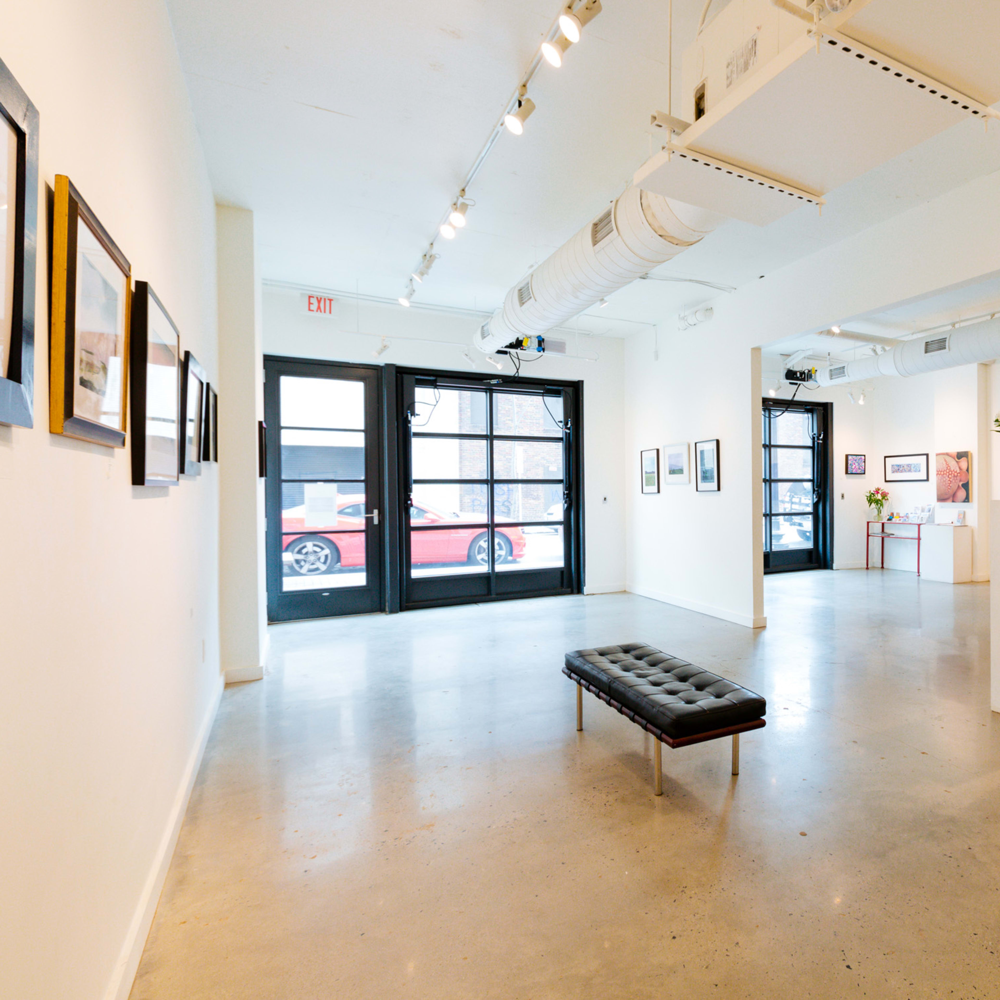 An art gallery featuring white walls, a polished concrete floor, and a central black bench with framed artwork displayed around the space.