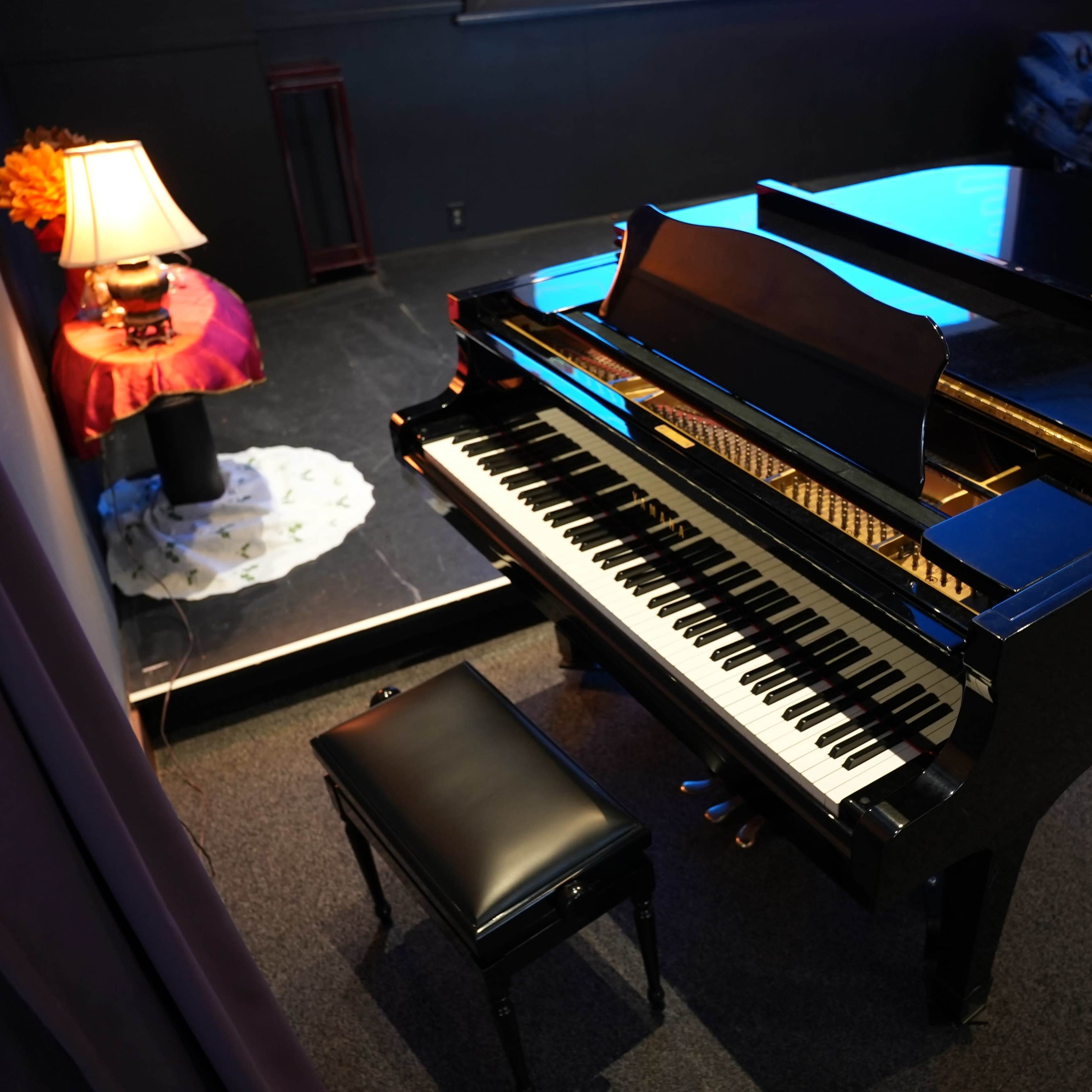 A black grand piano with a matching bench is positioned on a stage beside a decorated Christmas tree and a lamp.