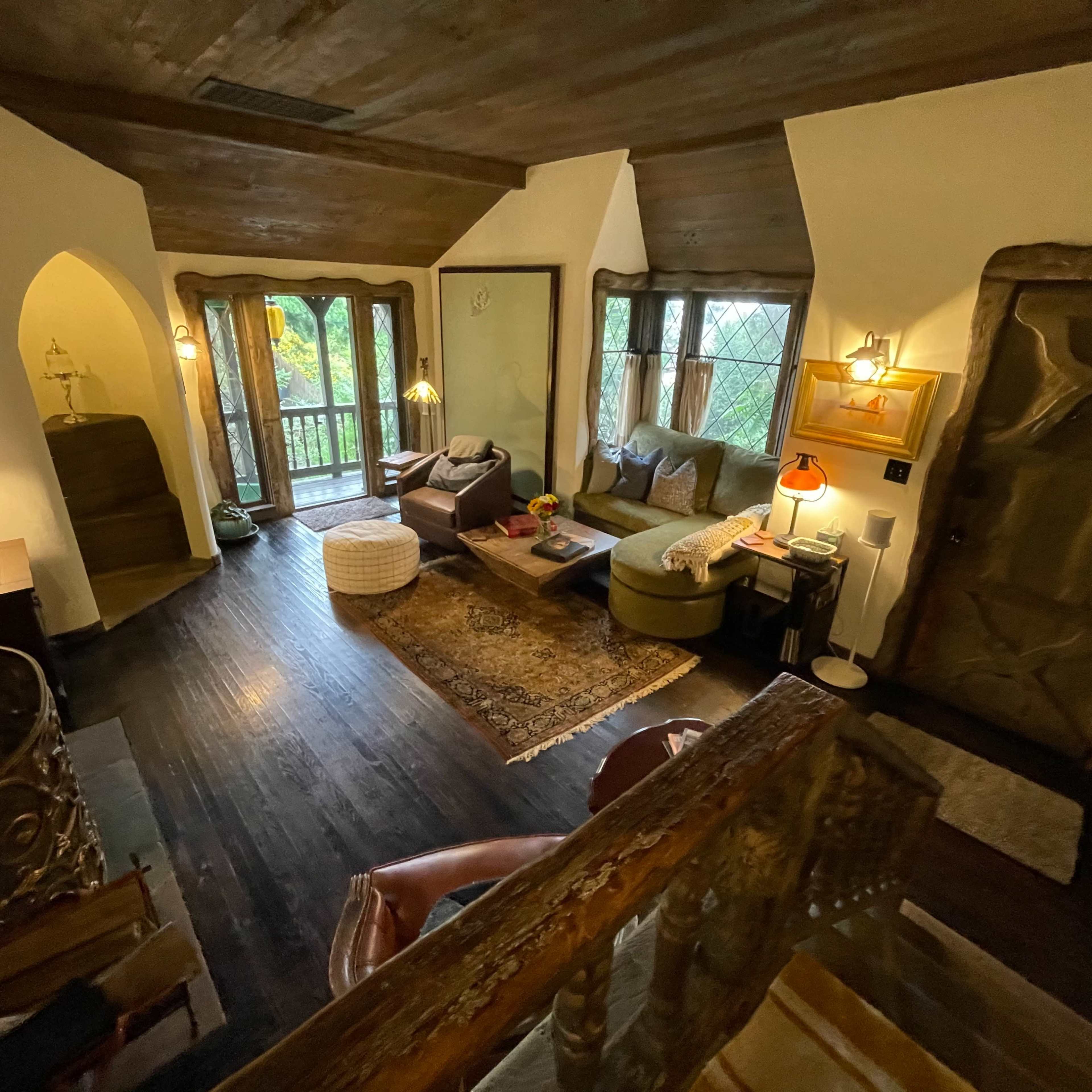 A cozy living room with large windows, wooden accents, and a staircase leading to an upper level.