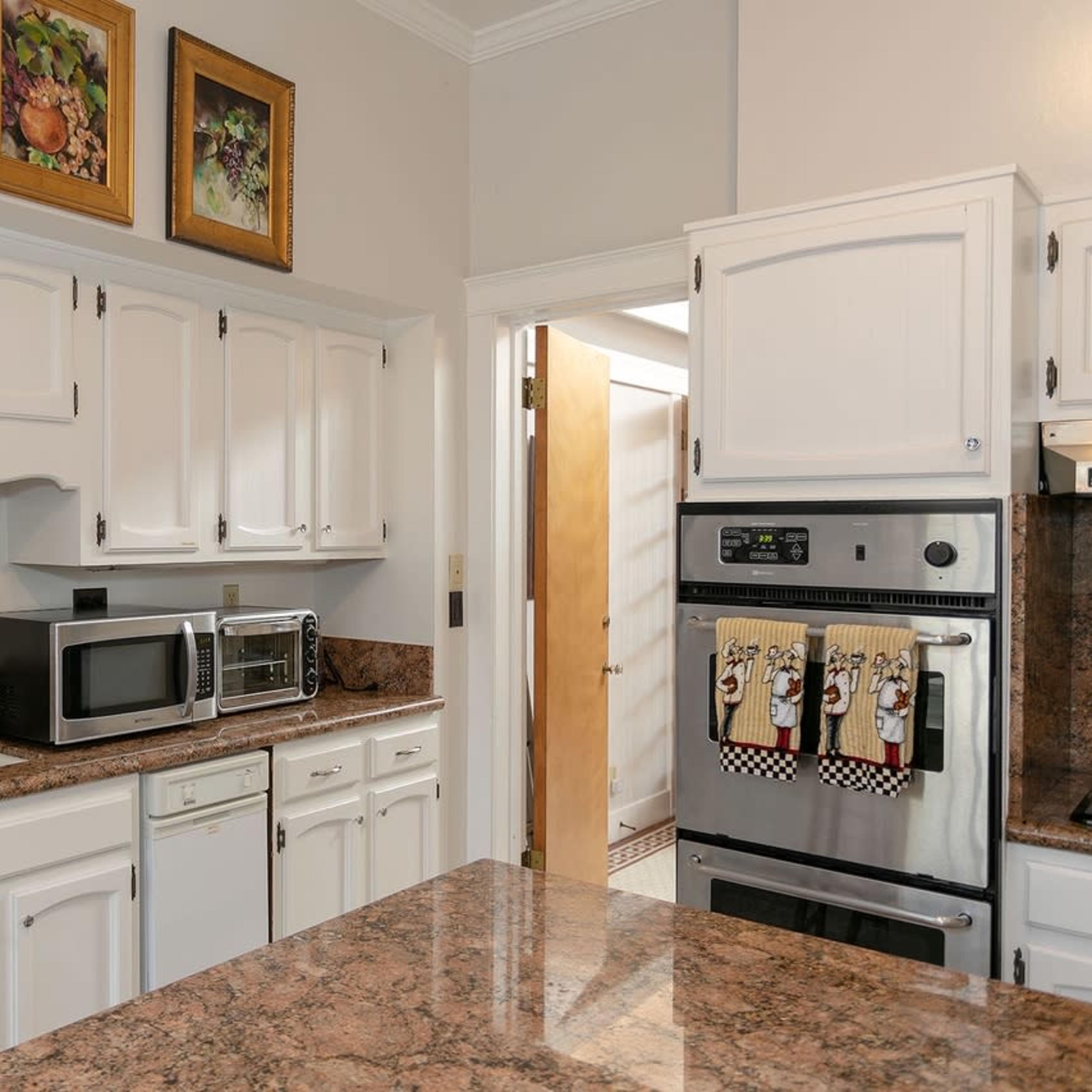 A kitchen features white cabinetry, a granite countertop, and appliances including a microwave and an oven.