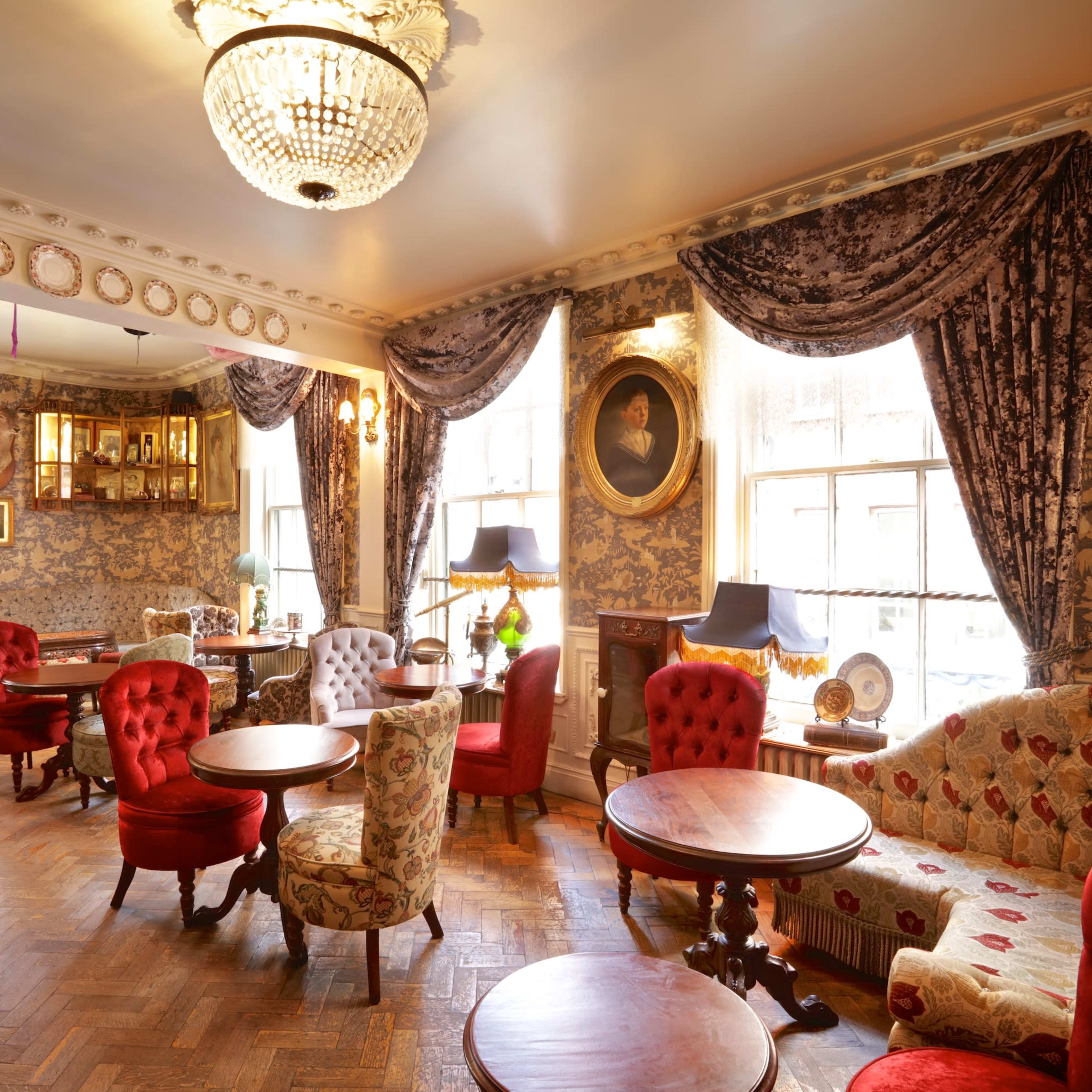 A cozy, elegantly decorated lounge area with patterned wallpaper, plush seating, and large windows allowing natural light.