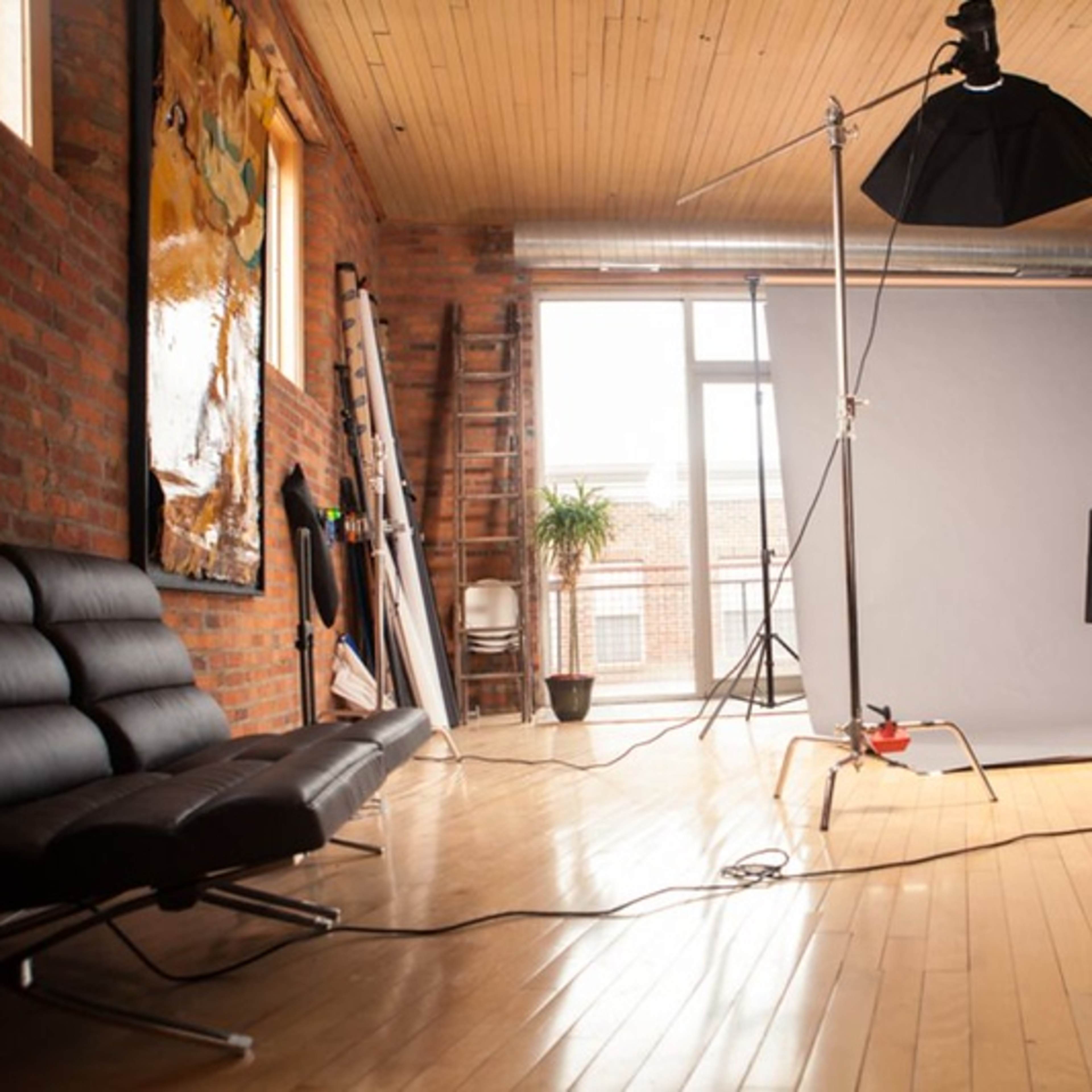 A photography studio with a backdrop, lighting equipment, and a black sofa against a brick wall.