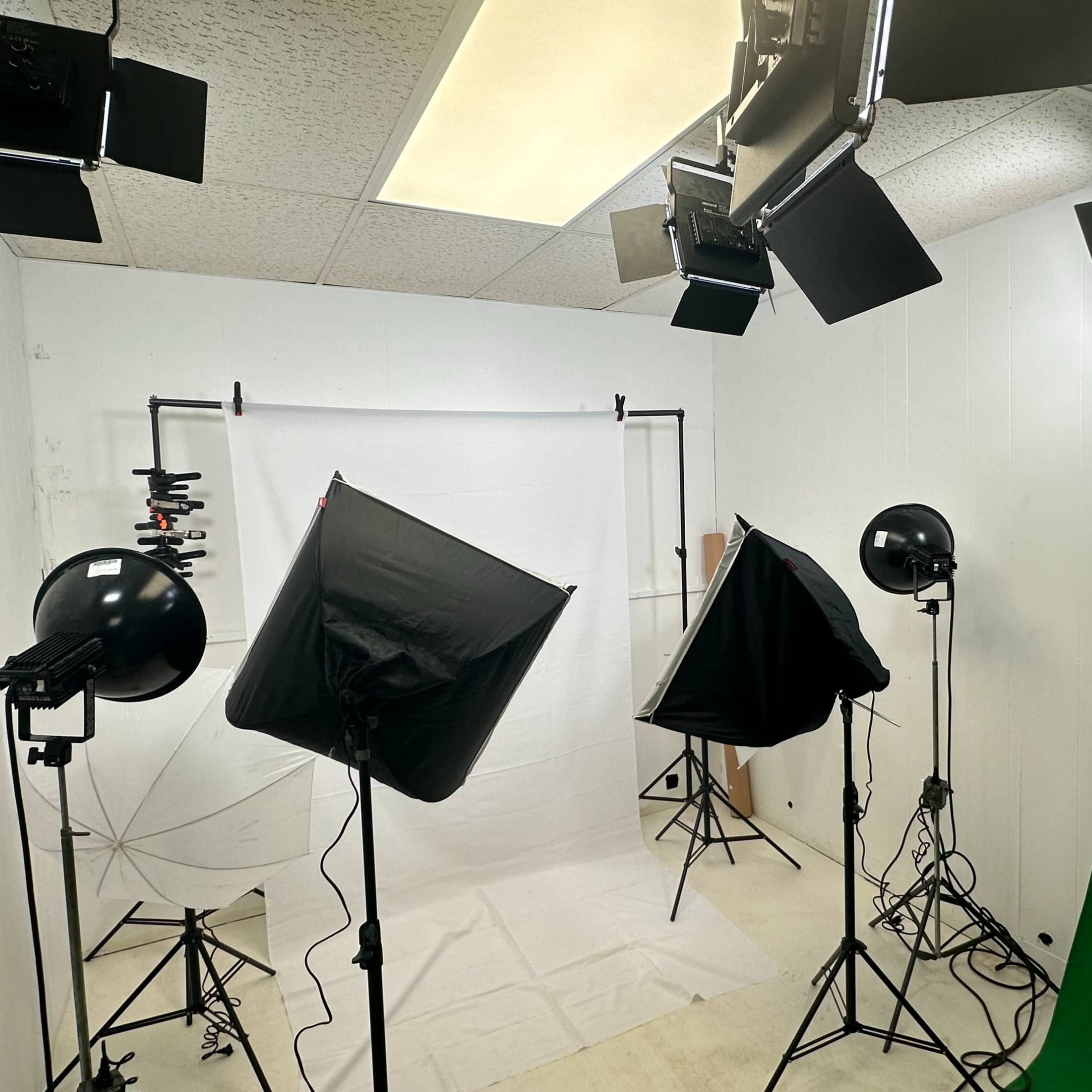 A photography studio equipped with various lighting setups, a white backdrop, and a green screen.