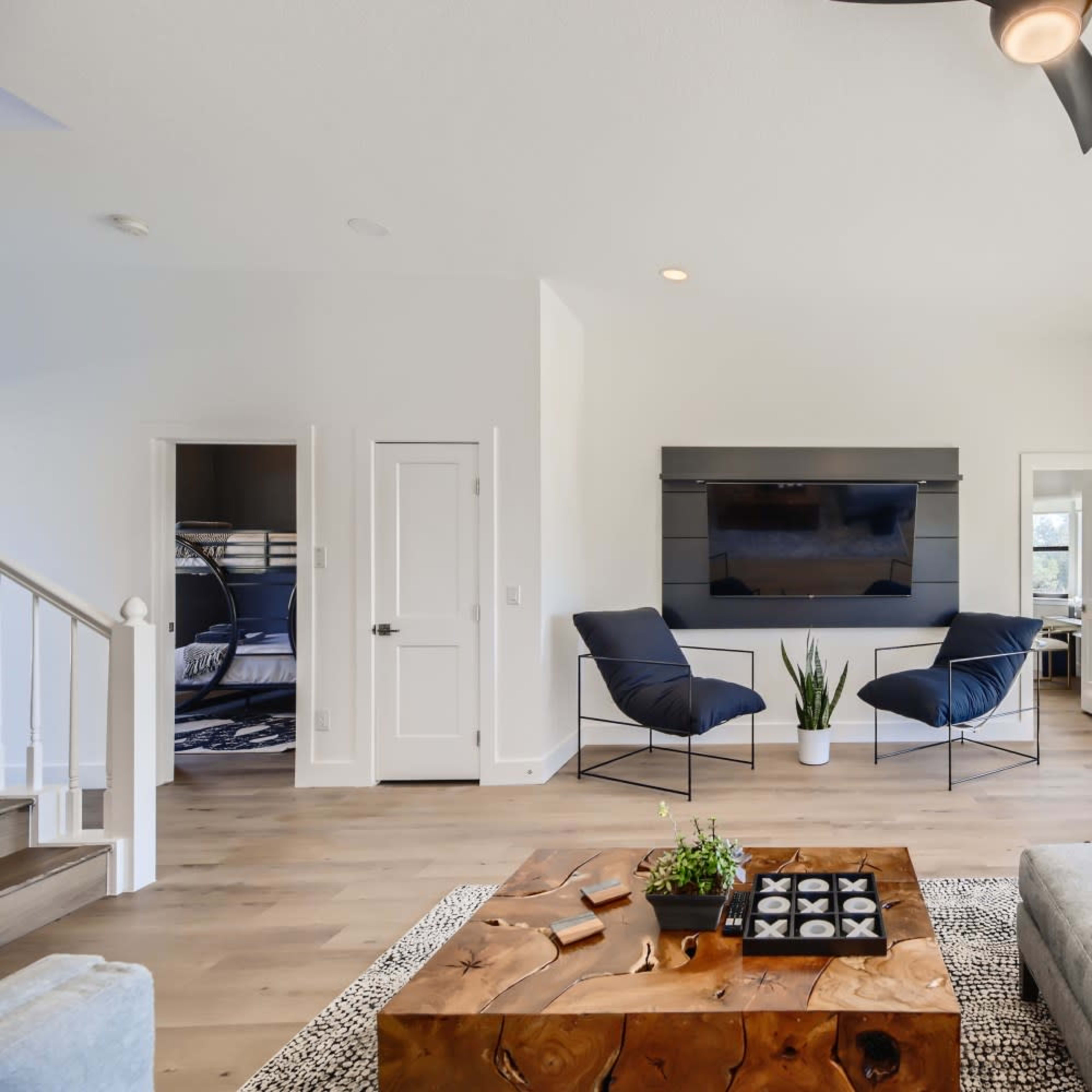 A modern living room with a light-colored curved sofa, a wooden coffee table, and two black chairs facing a wall-mounted television.