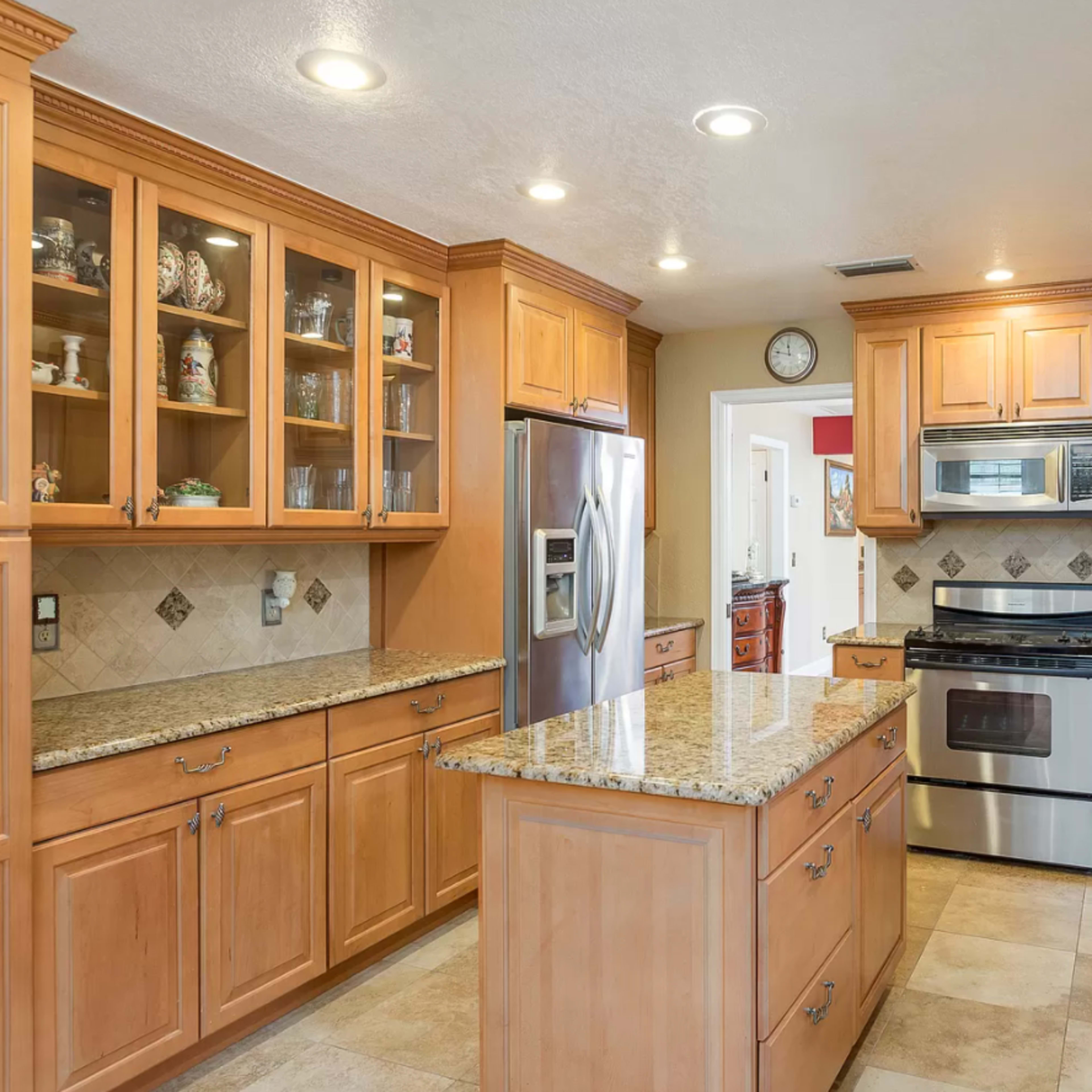 A modern kitchen features wooden cabinets, stainless steel appliances, and a large central island with a granite countertop.