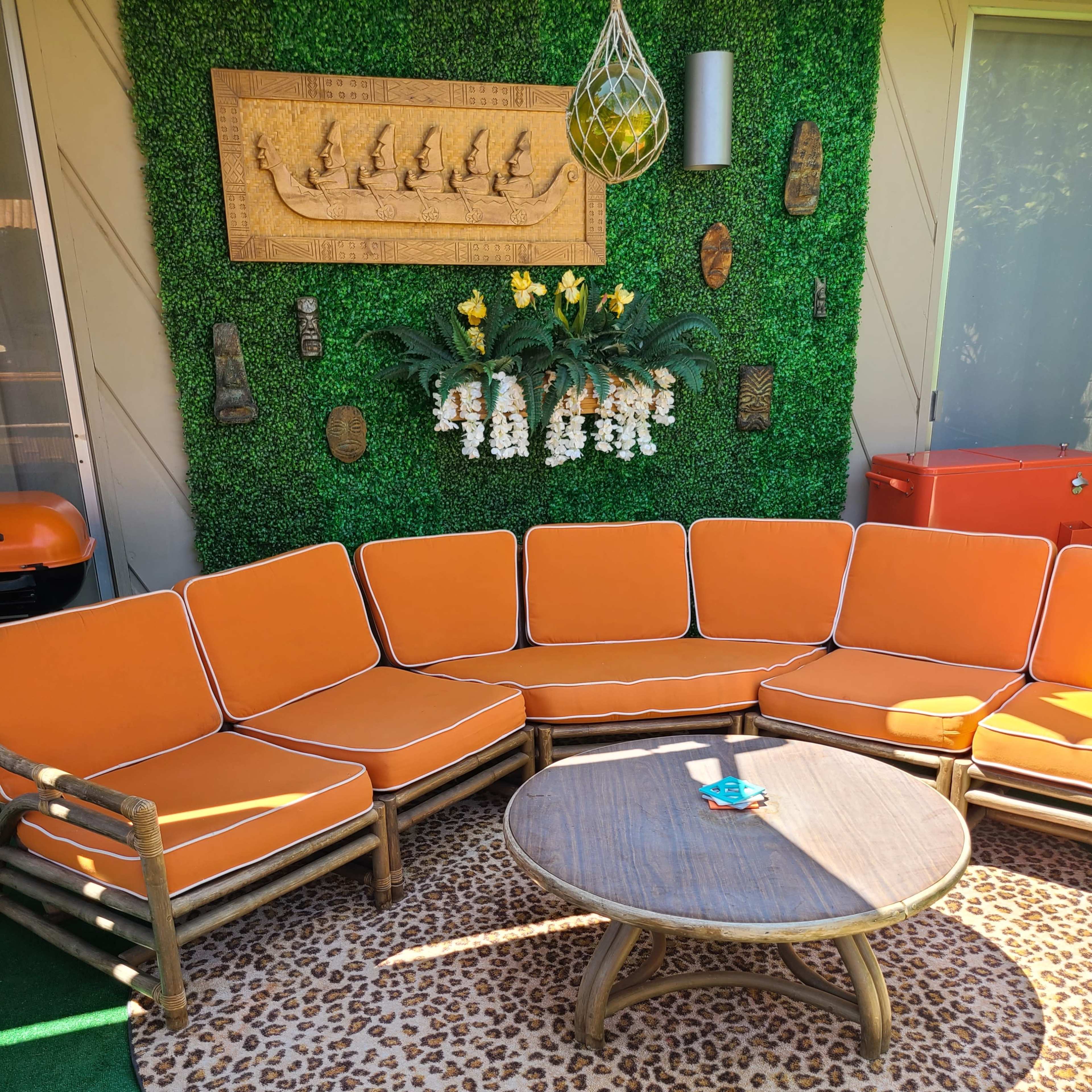 The scene features a circular leopard-print rug centered under a round wooden coffee table, surrounded by an orange, L-shaped sectional couch and decorative wall elements against a green backdrop.