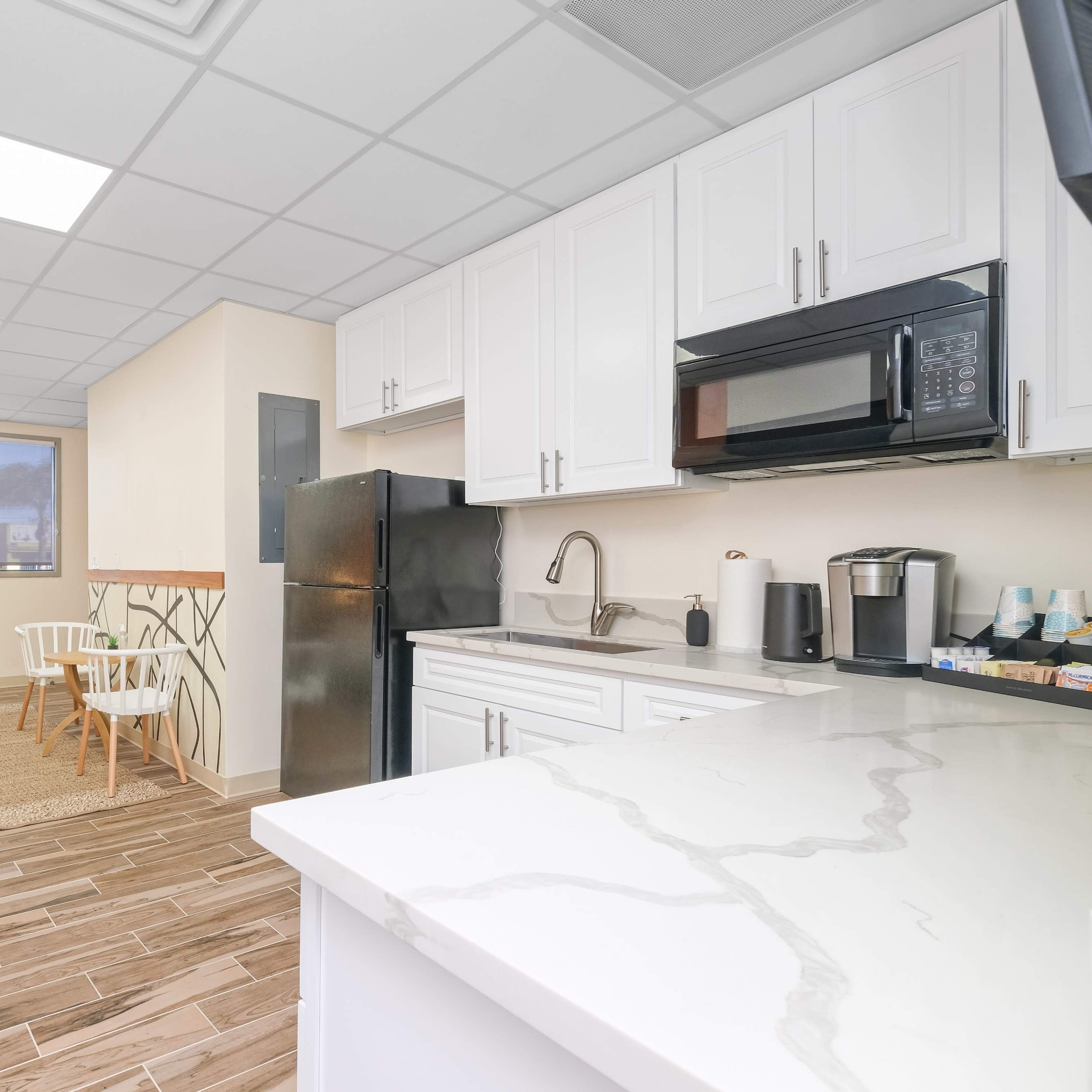 A modern kitchen and living area with white cabinets, a black refrigerator, and a cozy seating space featuring a couch and chairs.