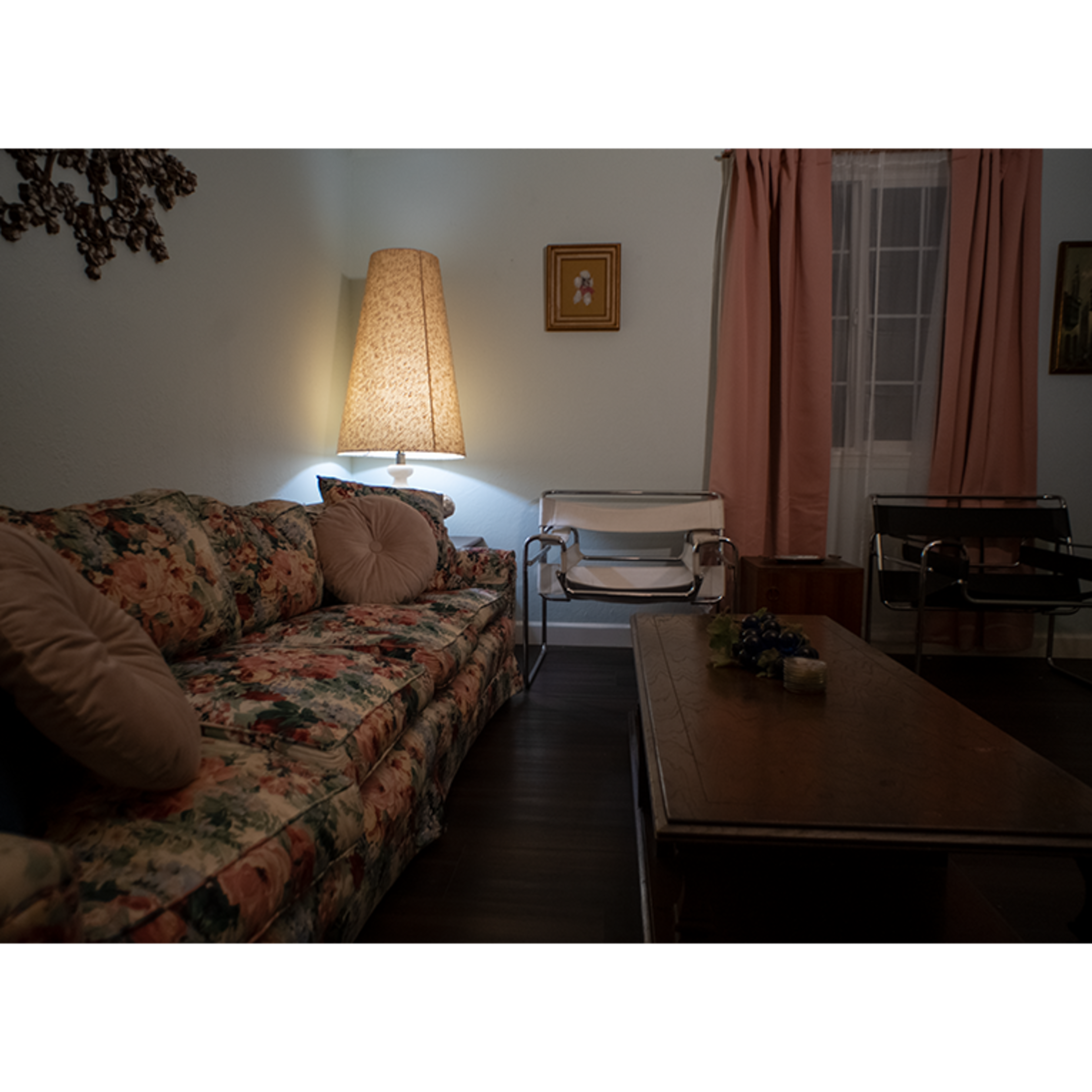 A cozy living room with a floral couch, a wooden coffee table, and a standing lamp casting soft light.