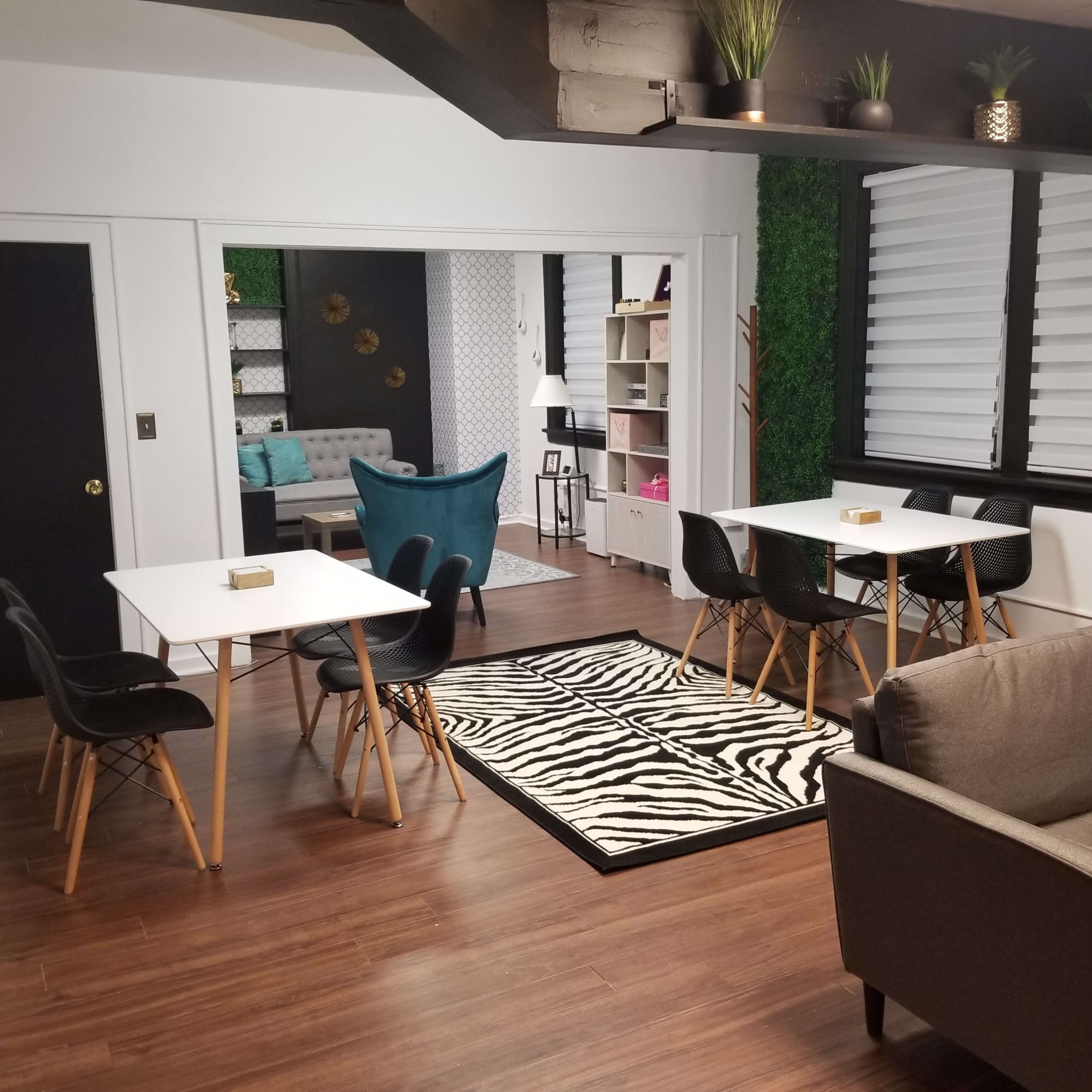 A modern multi-functional room featuring several tables and chairs, a couch, and a partitioned area with plants and decorative elements.