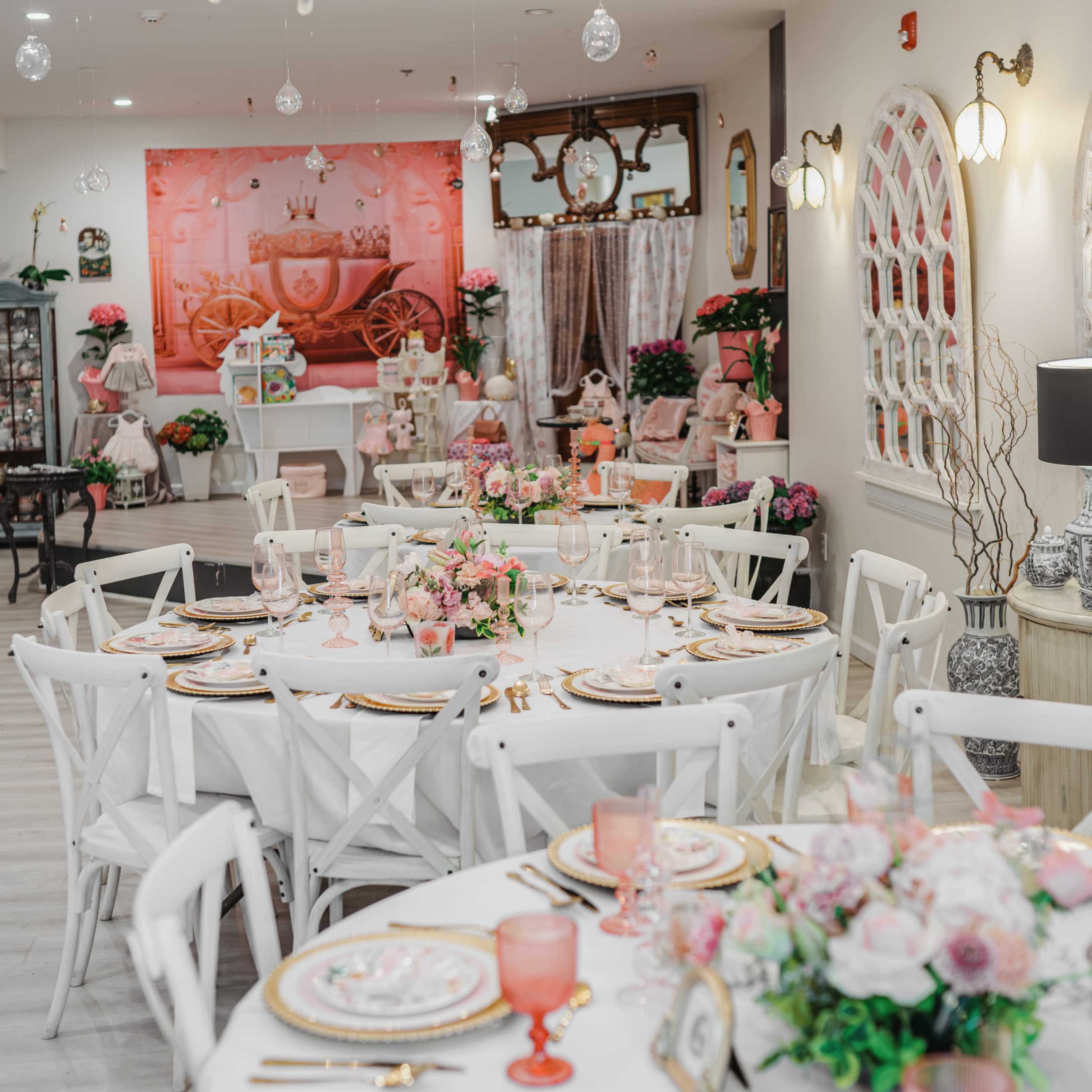 A beautifully arranged dining area features round tables set with floral centerpieces, elegant dishware, and a chandelier overhead in a bright, decorated space.