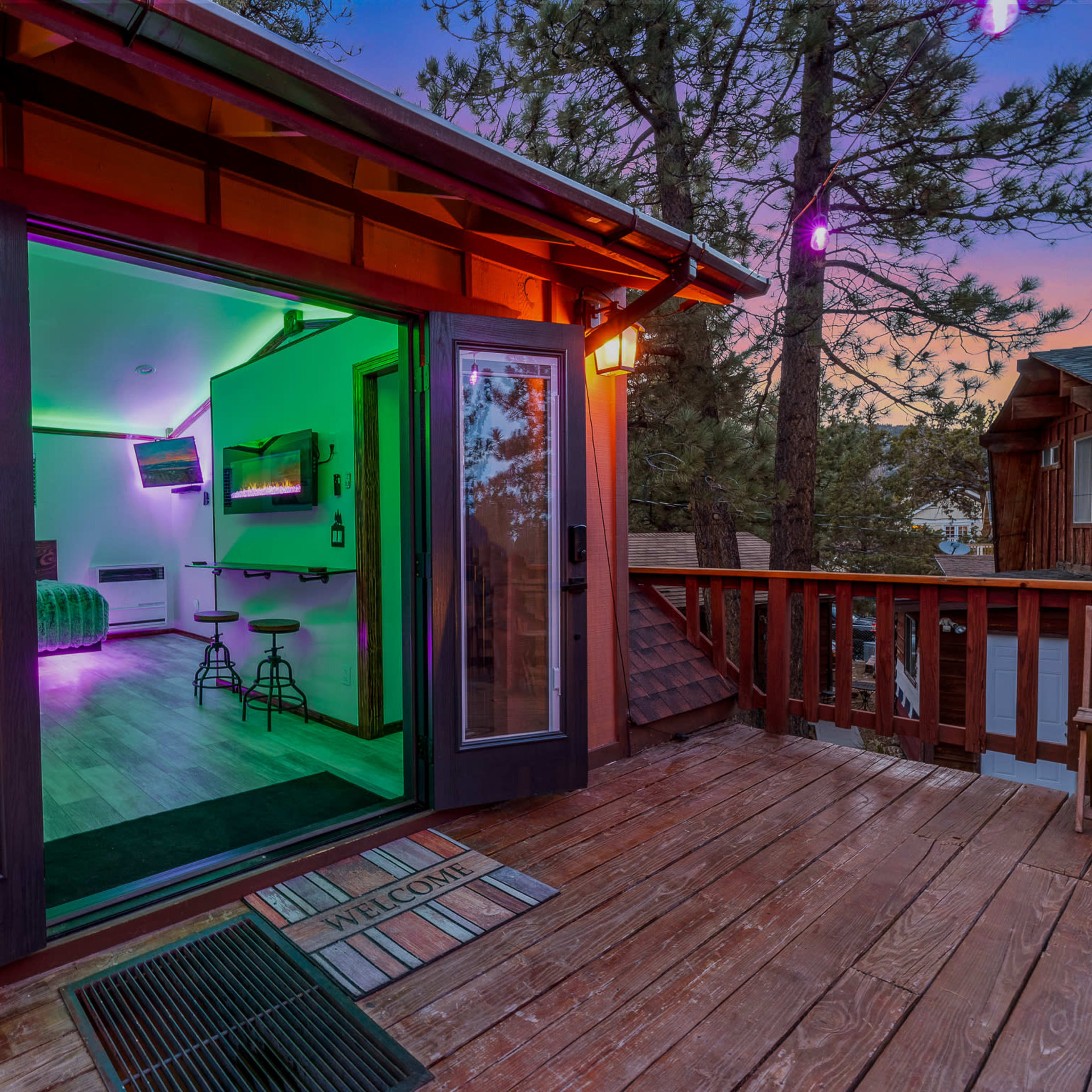 A doorway leads to a brightly lit room with modern decor, overlooking a wooden deck surrounded by trees.