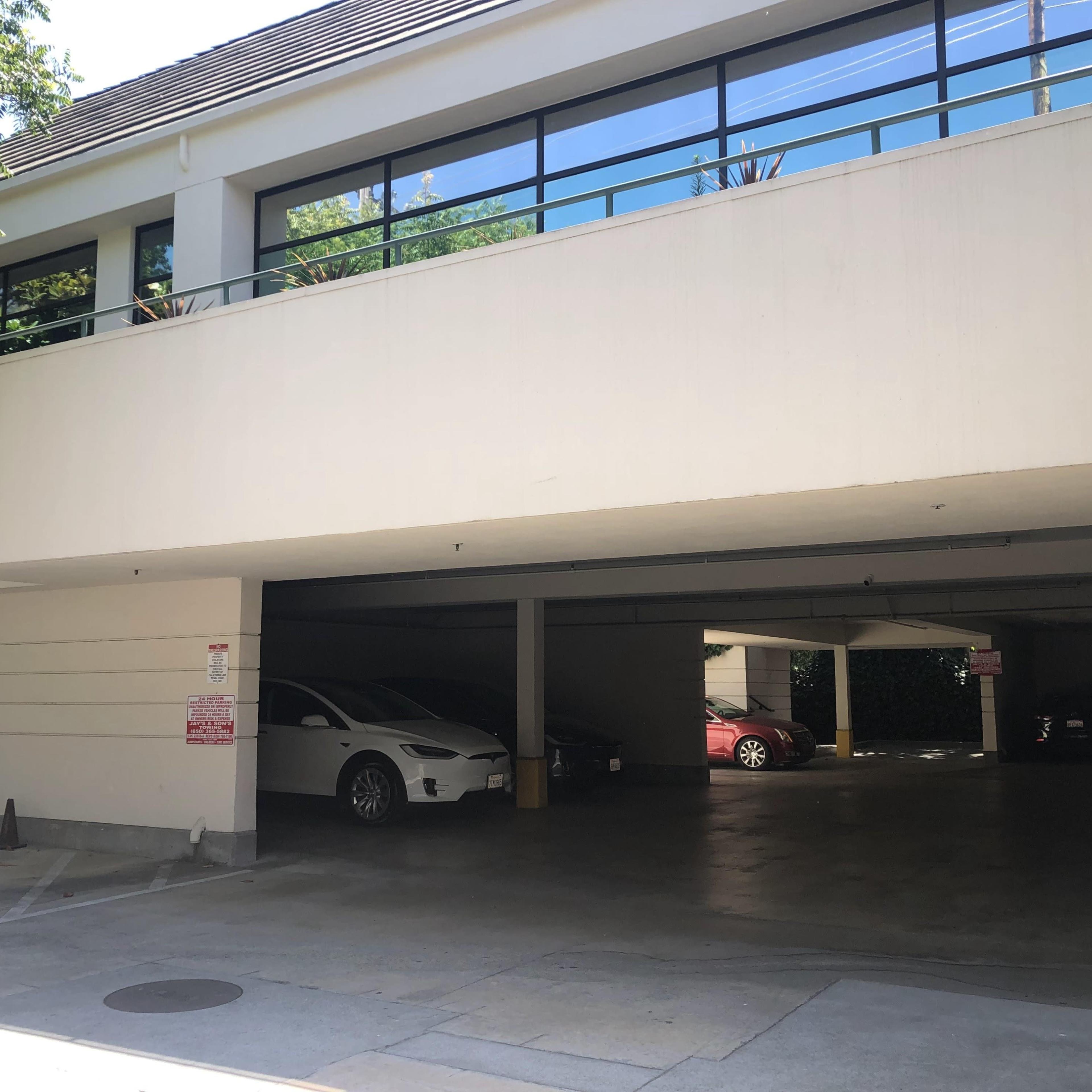 A partially shaded parking garage with two vehicles visible and a large window above.
