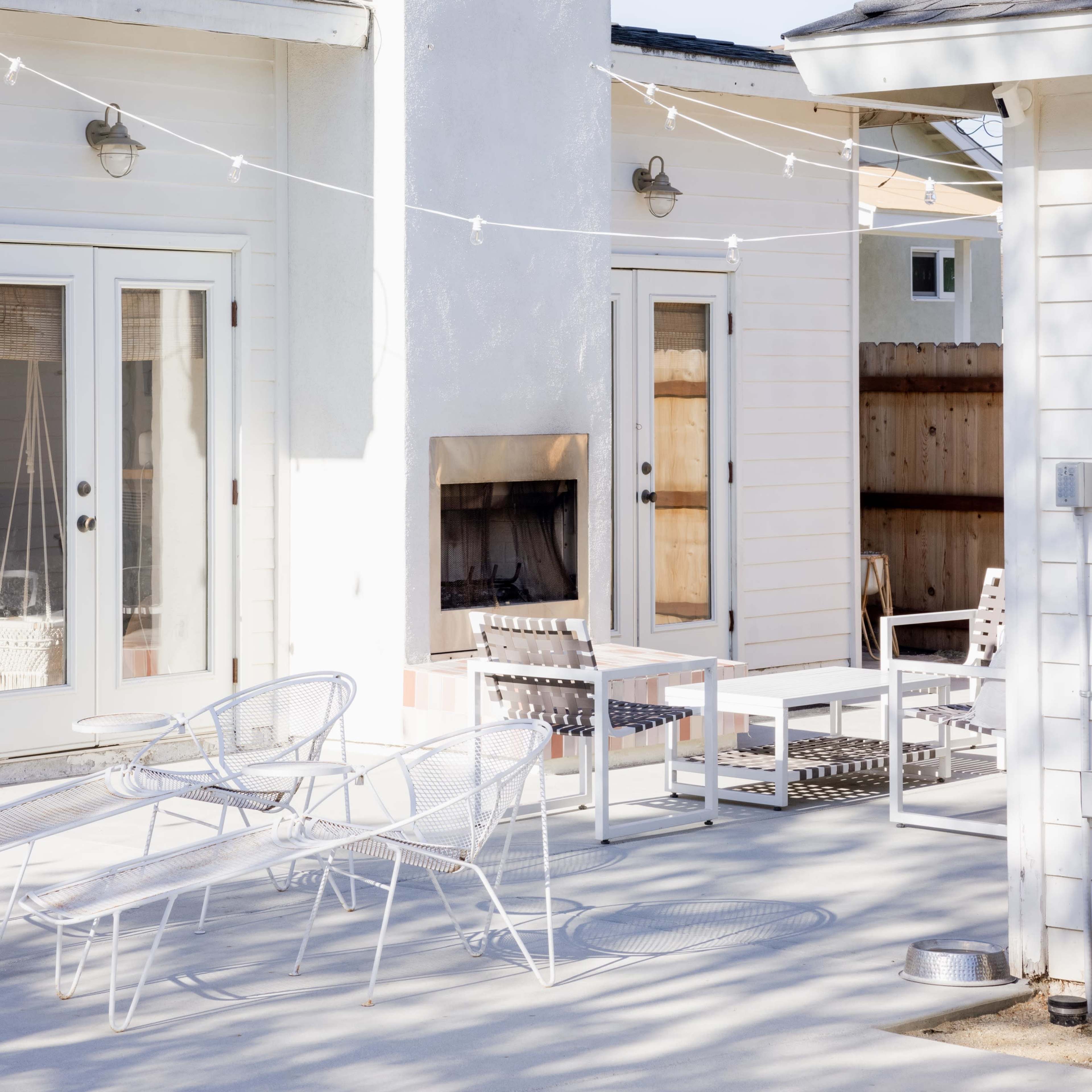 A modern outdoor patio area with a white chimney, a fireplace, and several white chairs arranged around a table.
