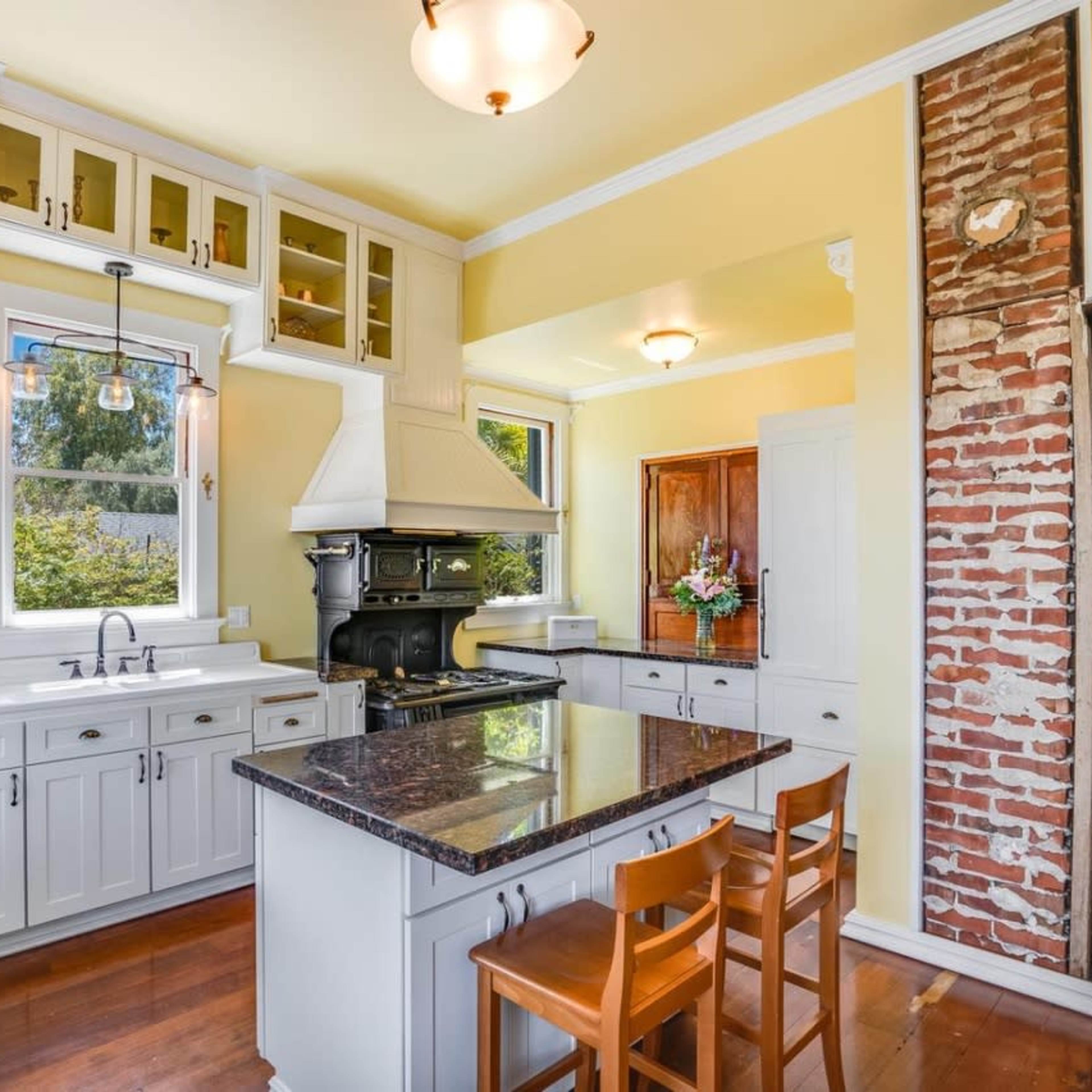 A kitchen with white cabinetry, a large island, a contrasting exposed brick wall, and modern appliances.