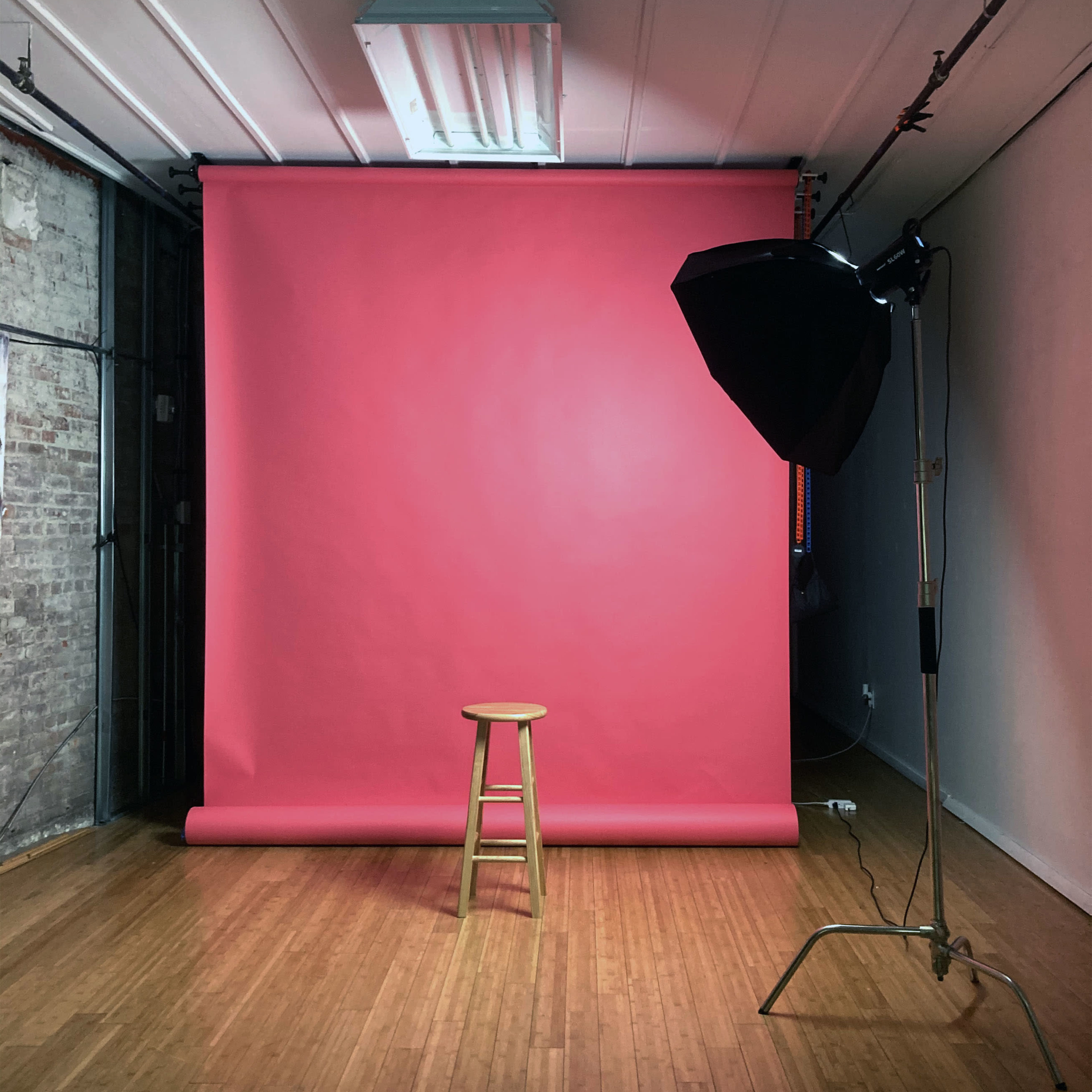 A wooden stool positioned in front of a pink backdrop with a lighting setup in a studio space.