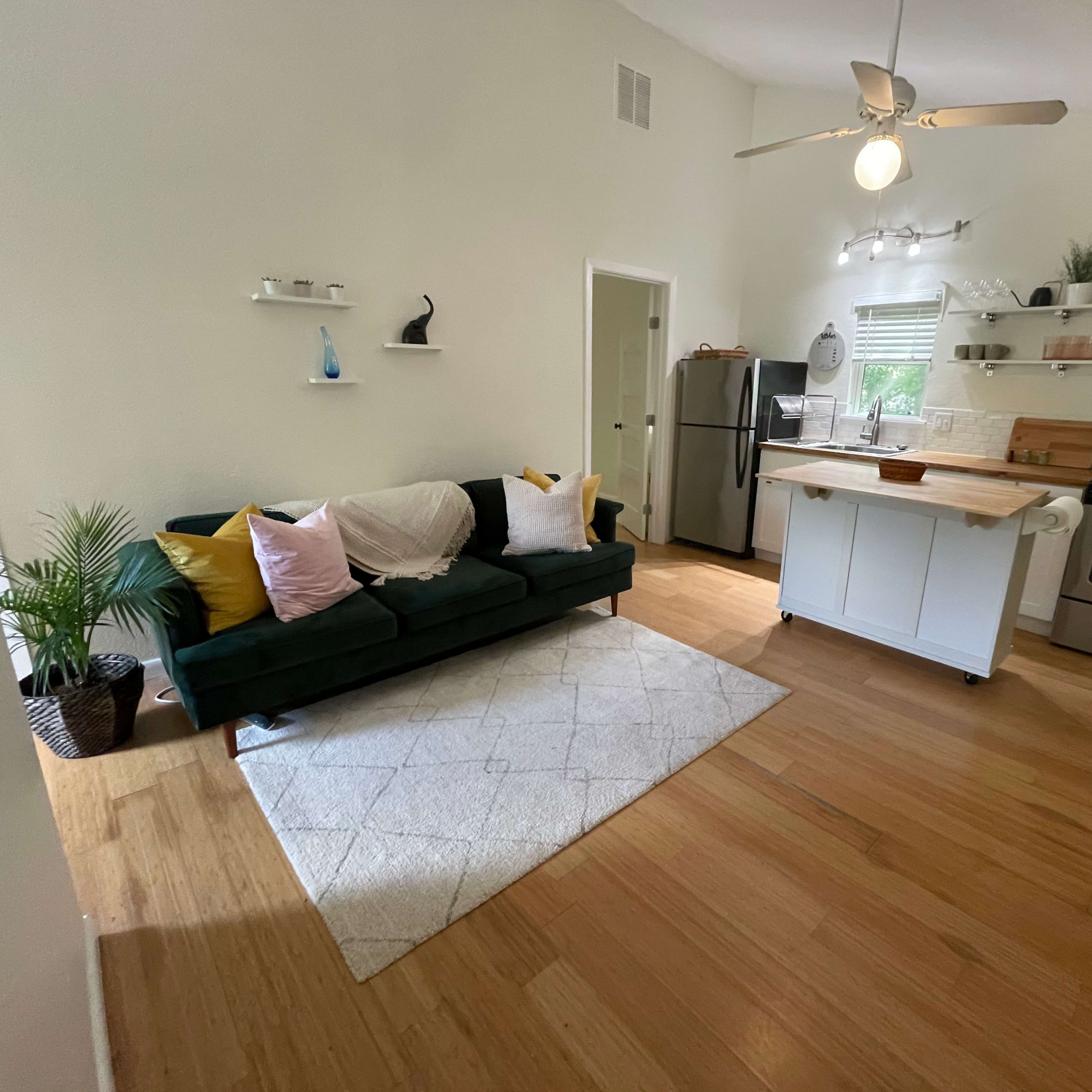 A compact kitchen and living area featuring a green couch, a small dining table, and modern appliances with a wooden countertop.
