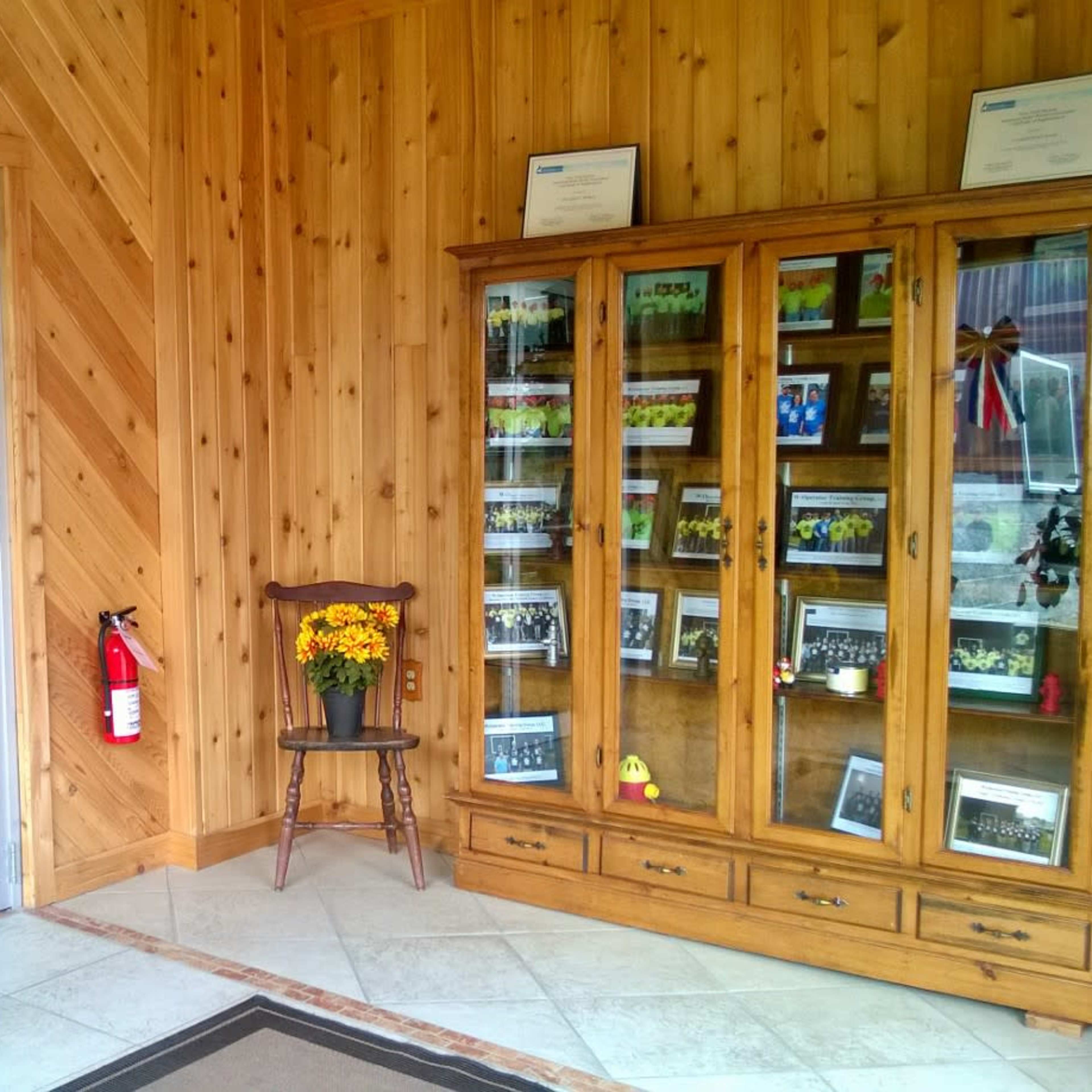 The entrance of the Port Watson Mini Conference Center, featuring double glass doors, a wooden display cabinet, and a chair with a vase of flowers against a wood-paneled wall.