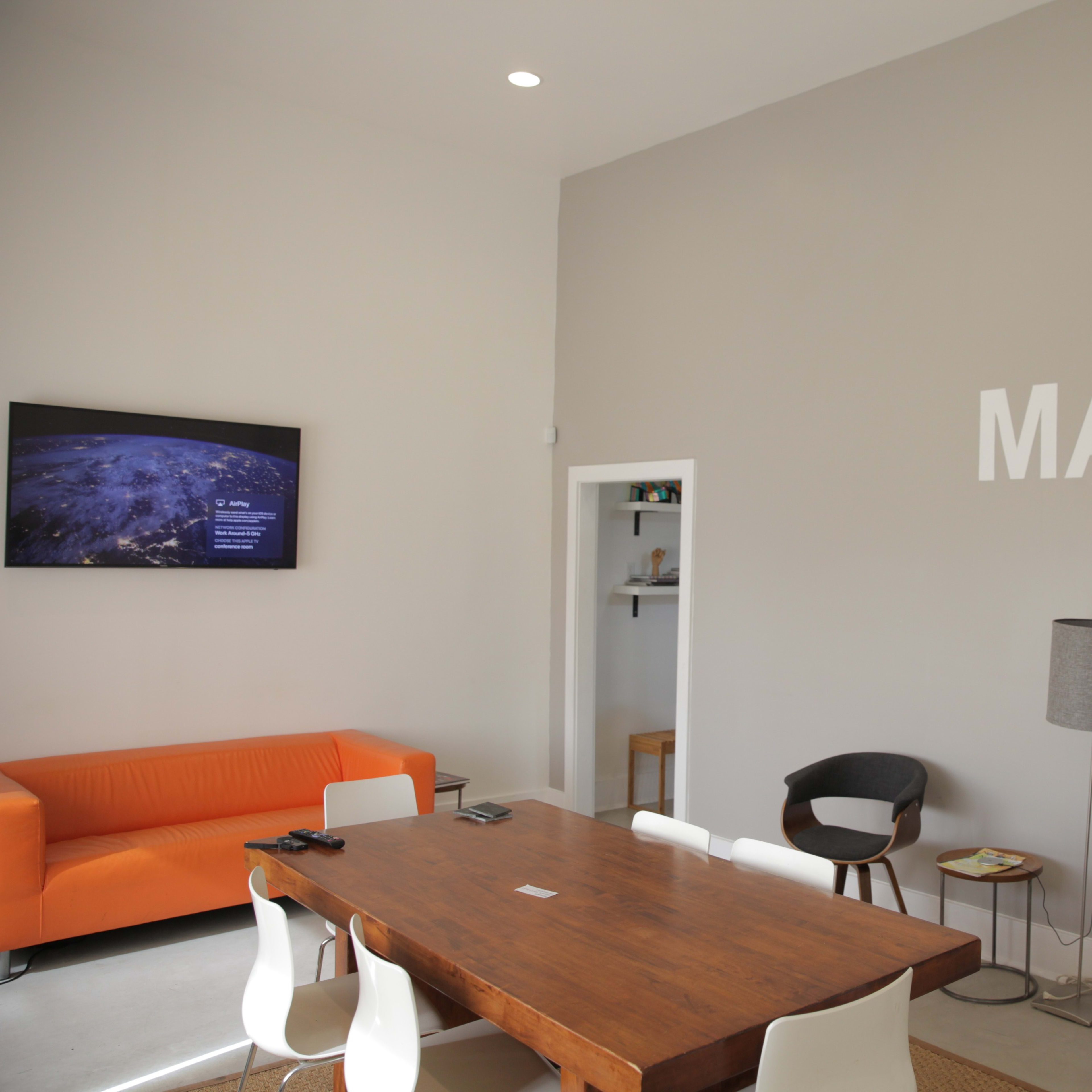 A modern lounge area features an orange sofa, a wooden table surrounded by chairs, and a wall with the phrase "MAKE IT MATTER" displayed prominently.
