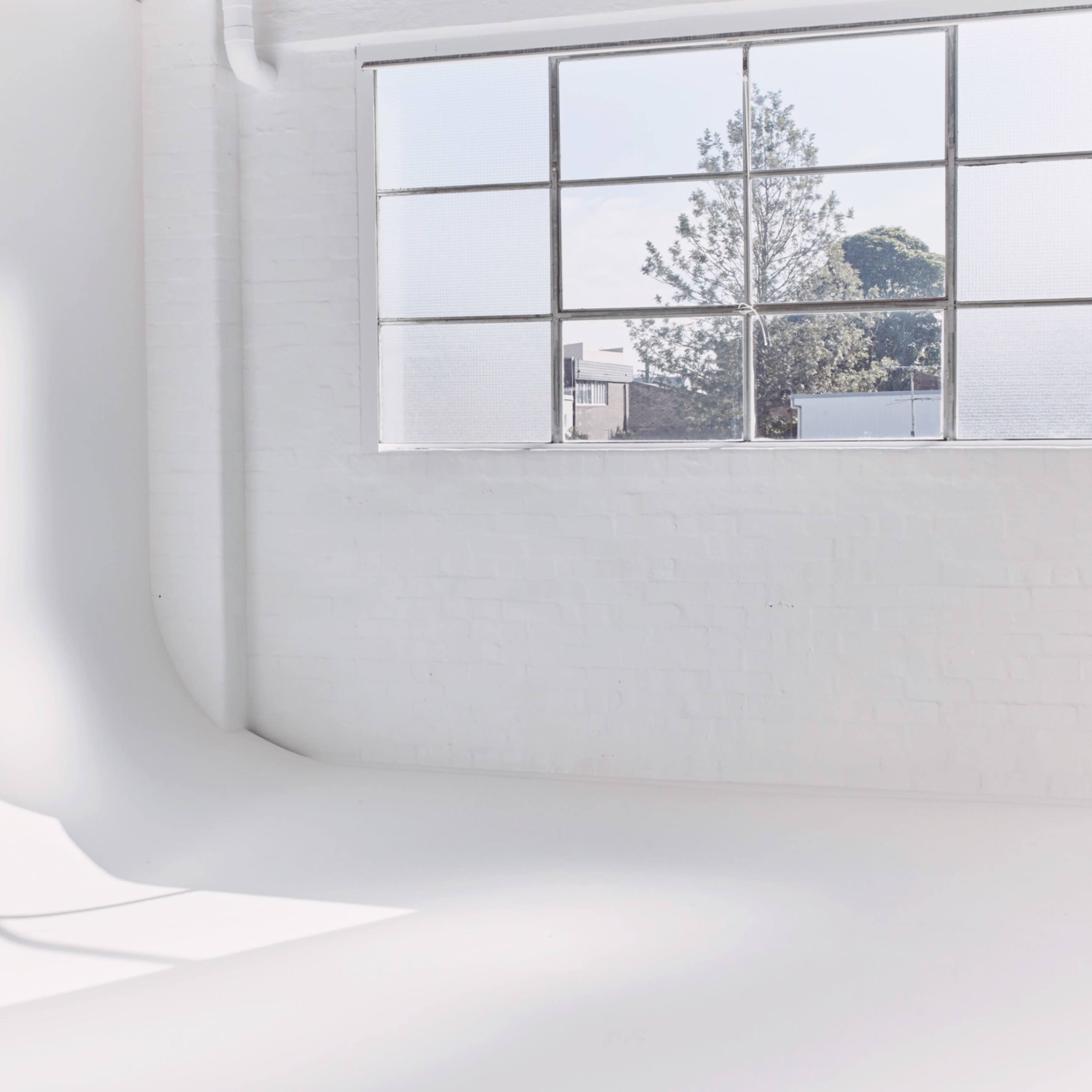 A bright, minimalist room with a large window casting shadows onto the curved white walls.