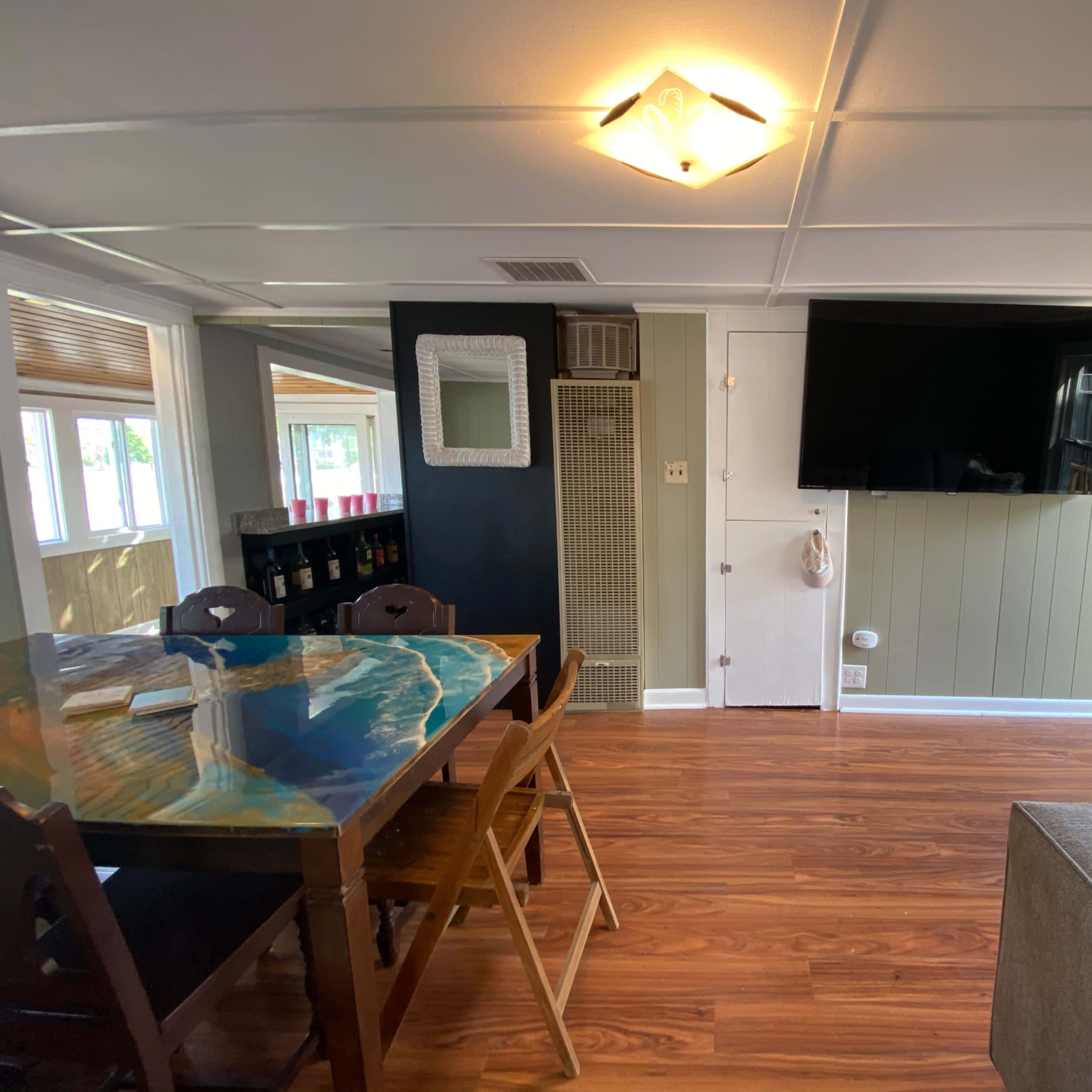 A modern living area with a dining table, a large wall-mounted television, and a door leading outside.