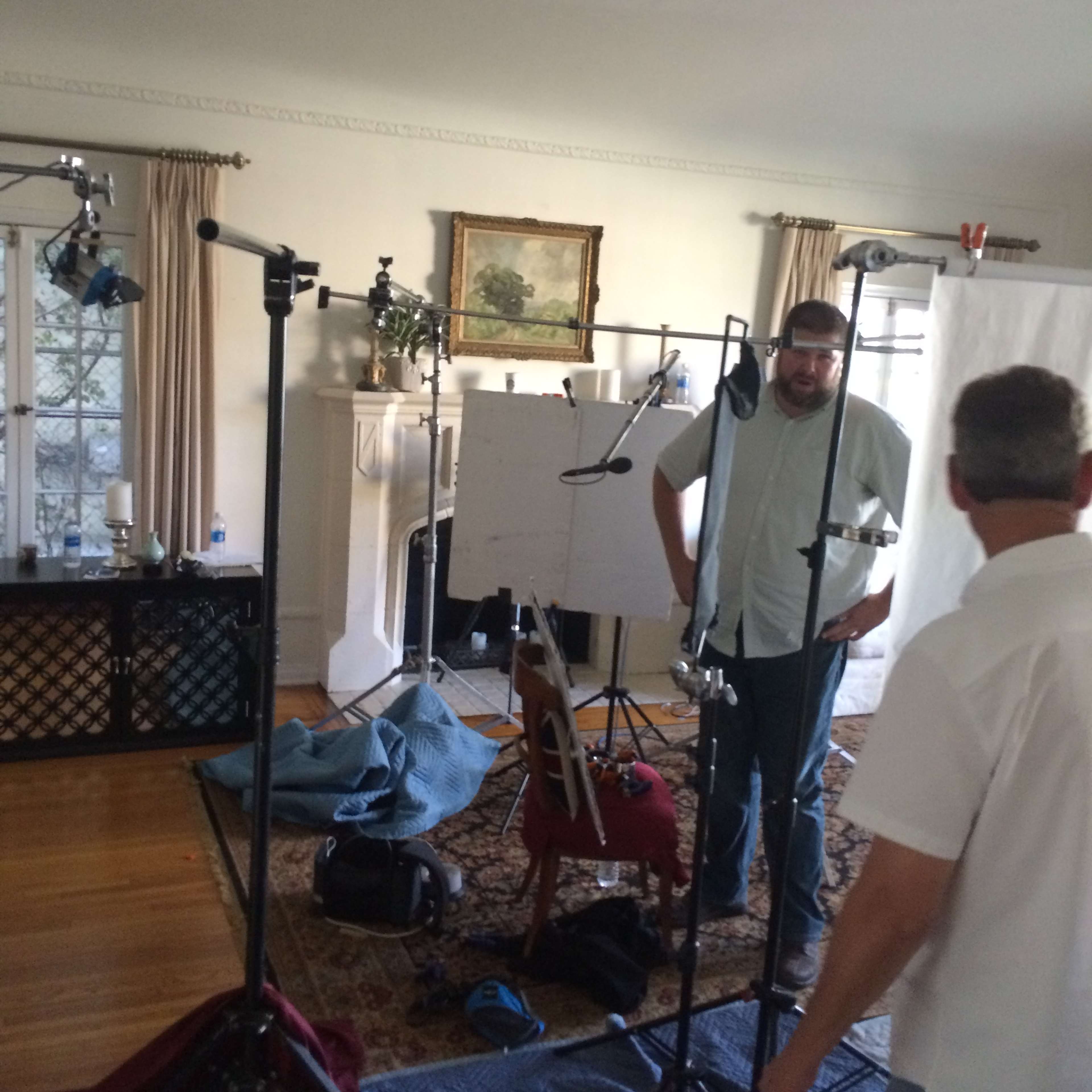 Two men standing in a room set up for a video shoot, surrounded by lighting equipment and a blank canvas on an easel.