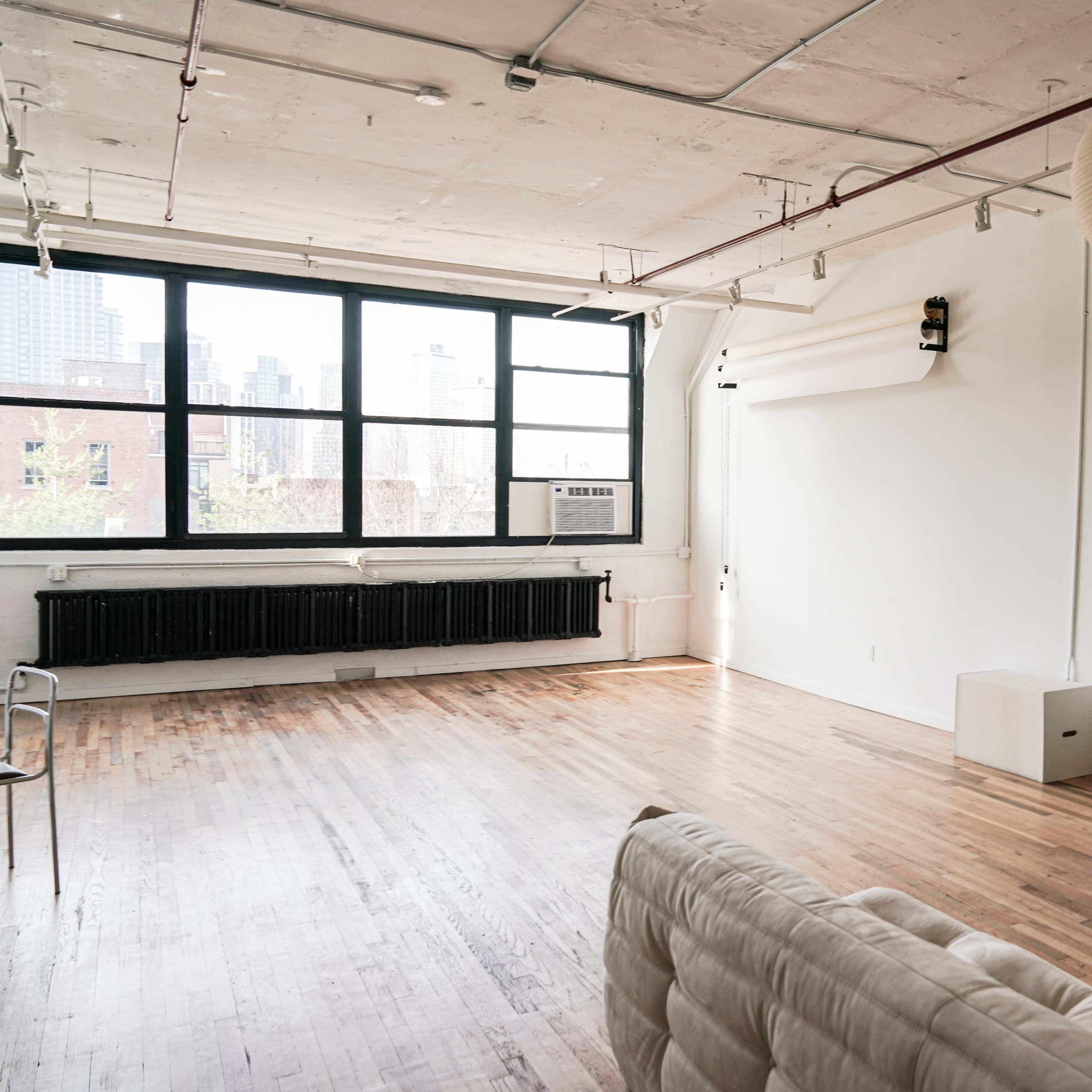 A spacious, minimalist room with hardwood floors, large windows, and a green-framed mirror against a white wall.