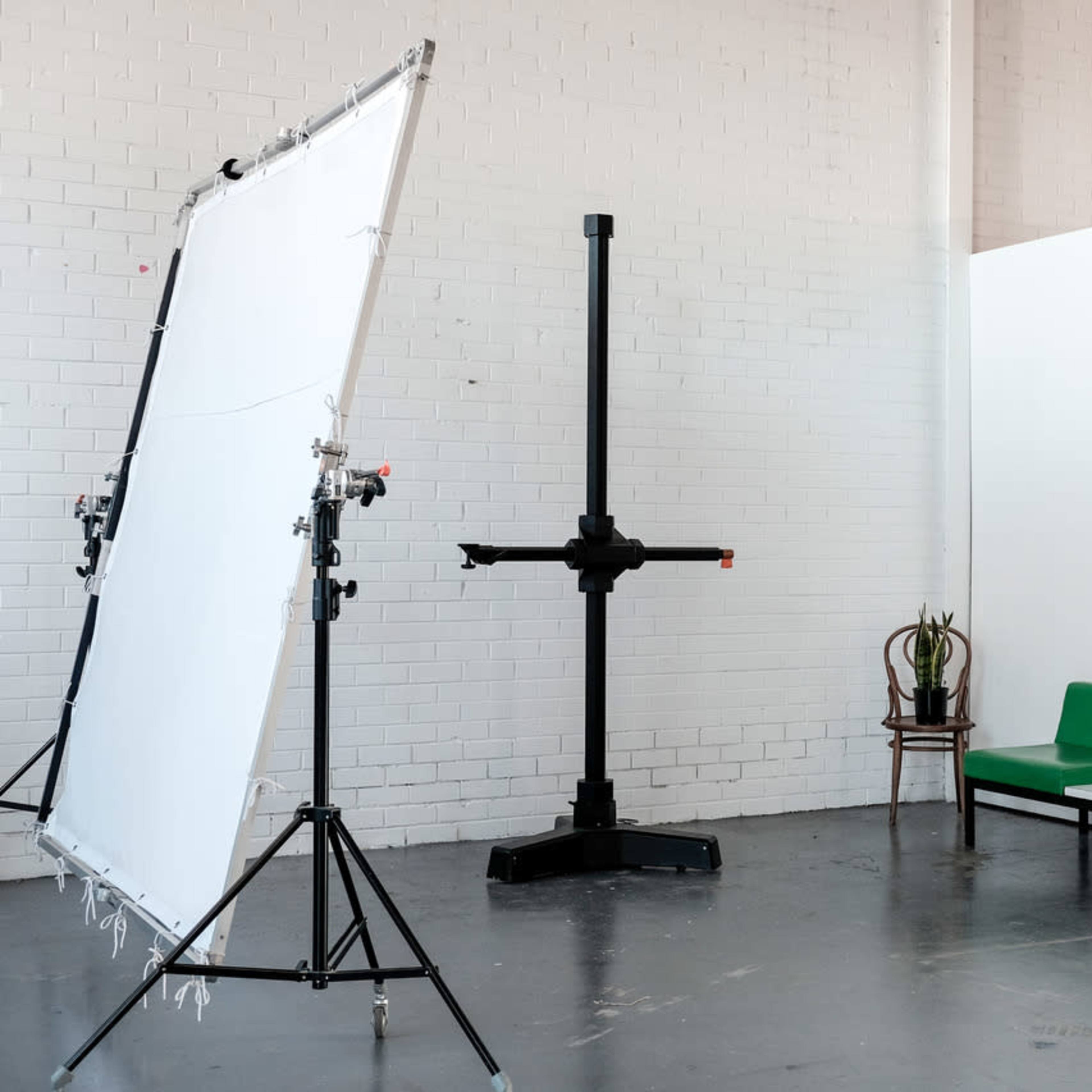 A minimalist photo studio featuring a large white backdrop, a support stand, two green benches, and a potted plant.