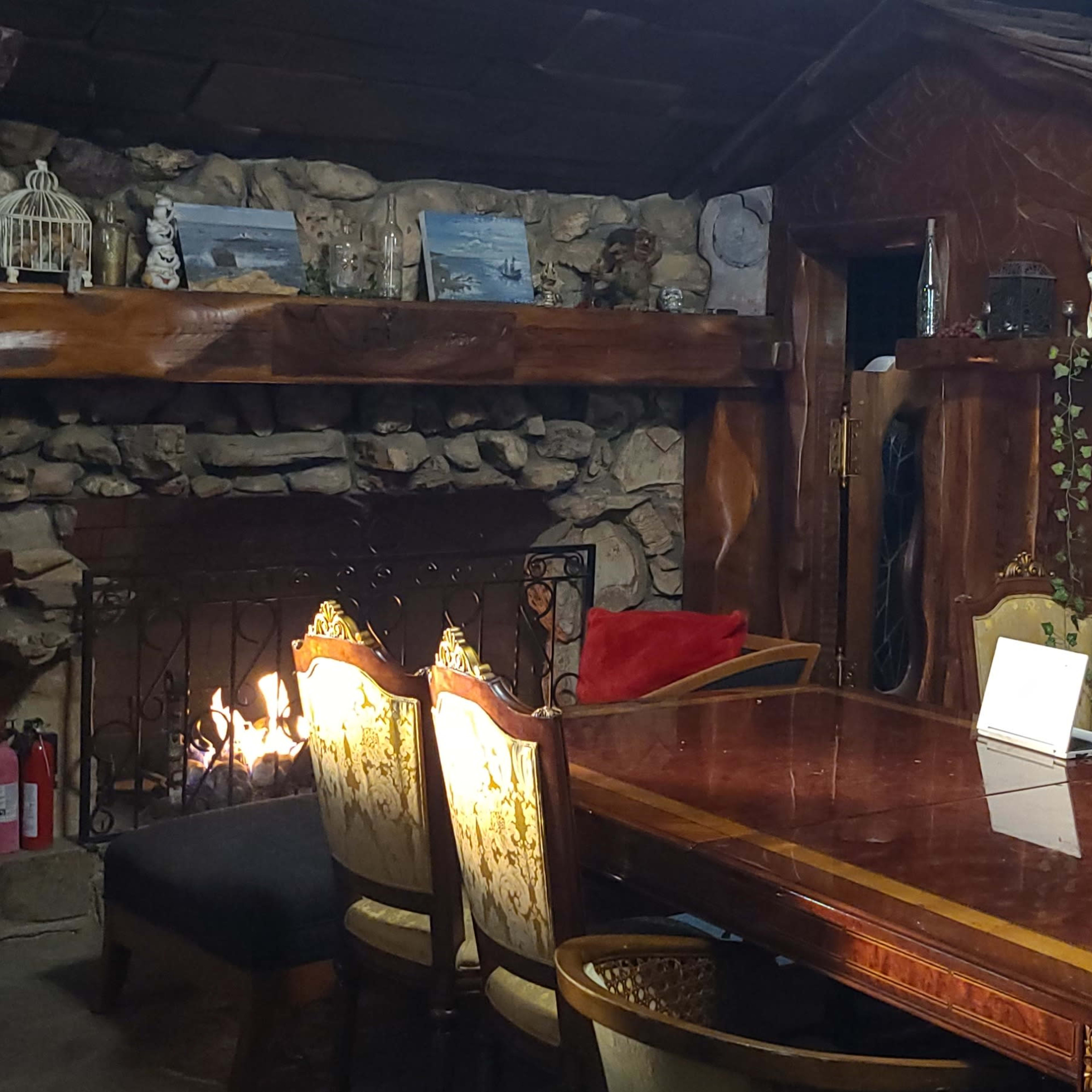 A rustic dining area features a wooden table surrounded by upholstered chairs, with a stone fireplace and carved wood walls.