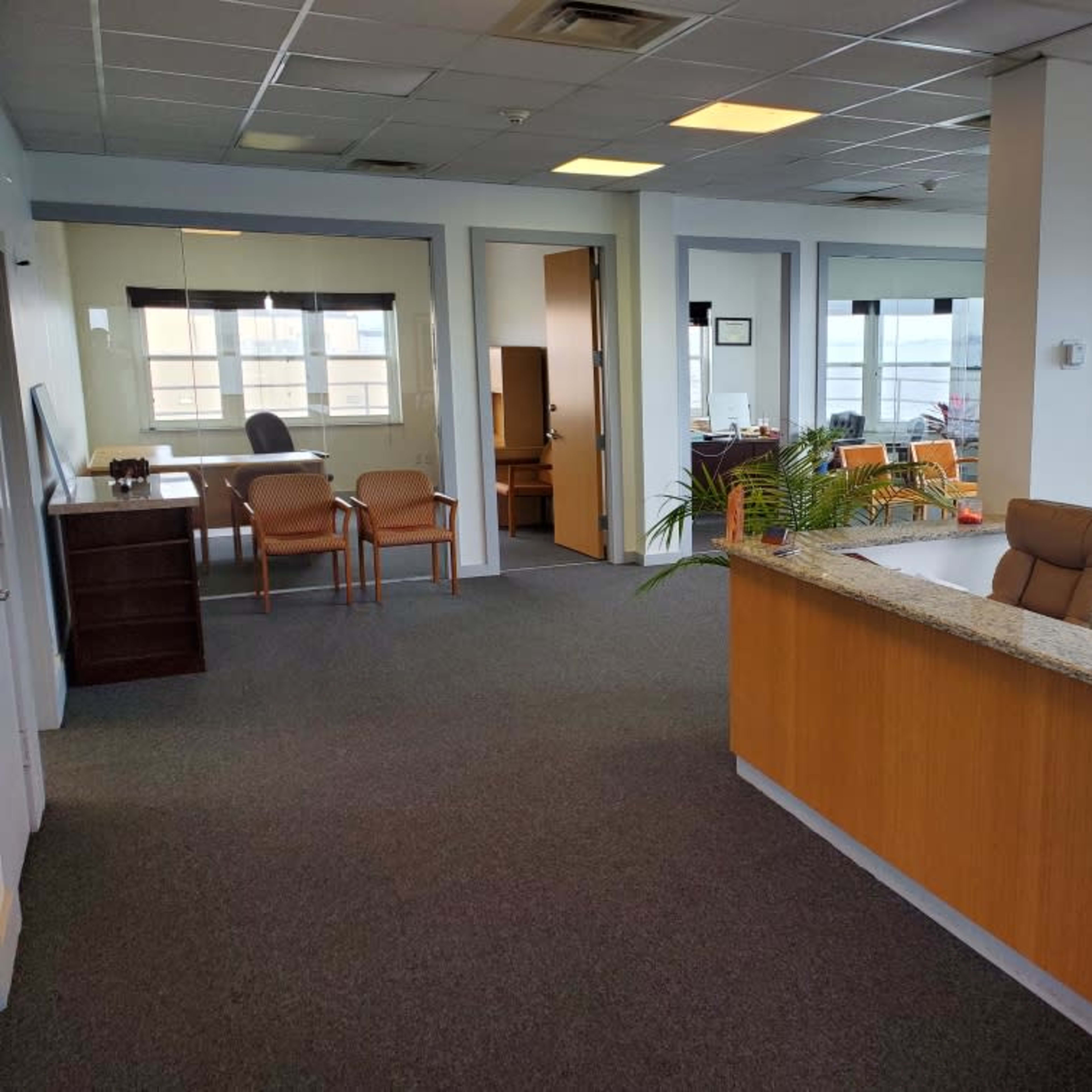 An office reception area with a front desk, chairs, and several office rooms visible in the background.