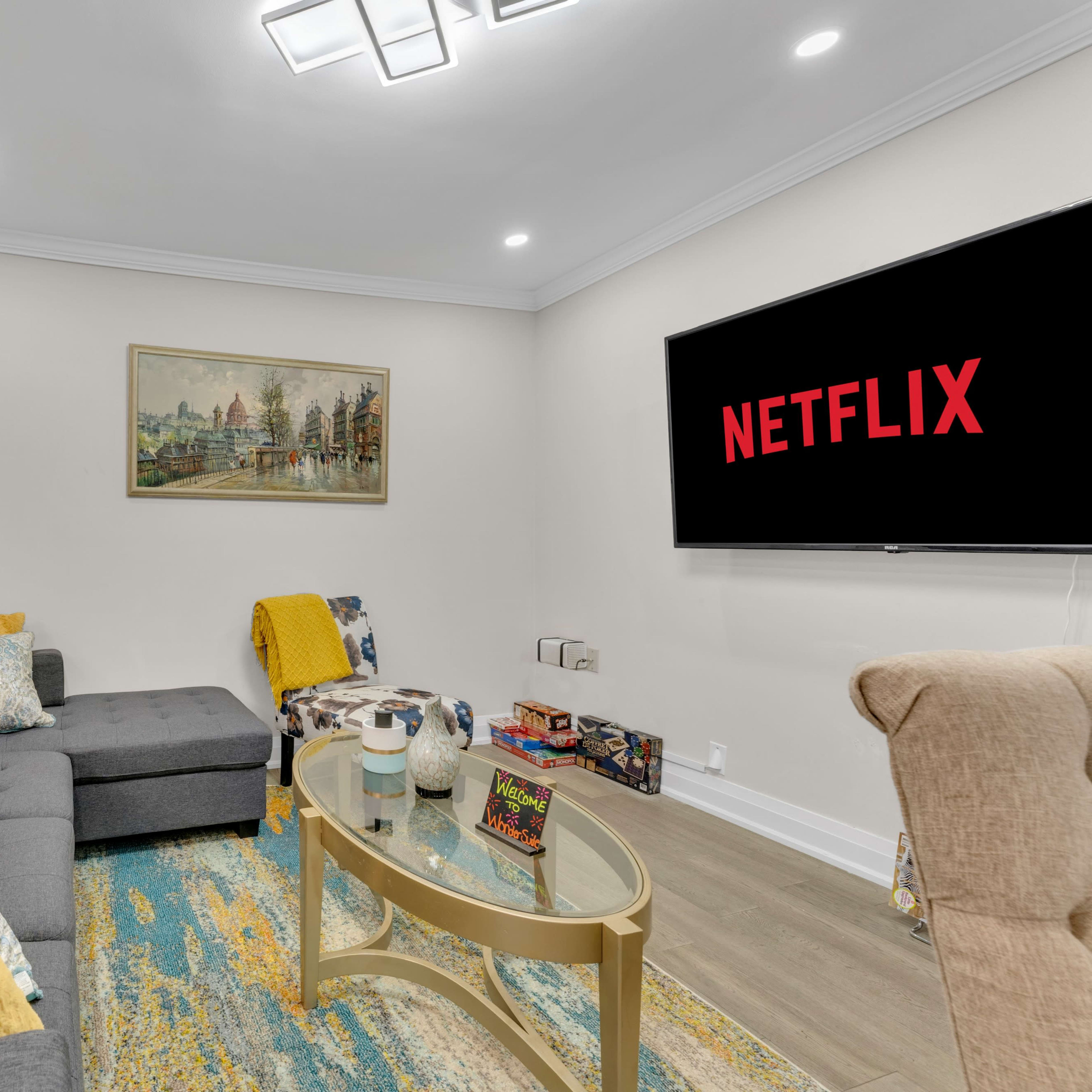 A modern living room features a gray sectional sofa, a glass coffee table, and a large television displaying the Netflix logo.
