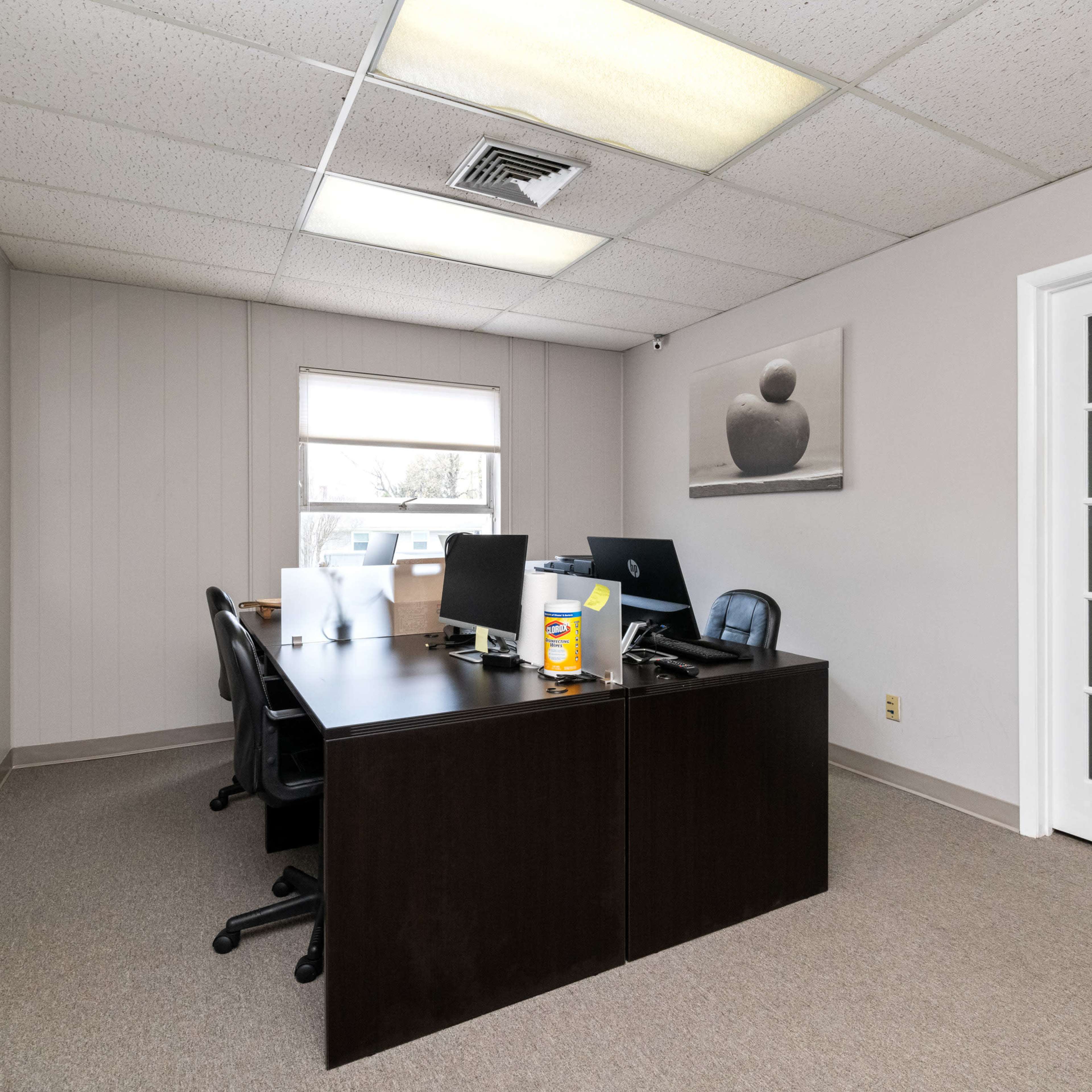 A sparsely furnished office with a large desk, two computer monitors, and a glass door leading to another room.