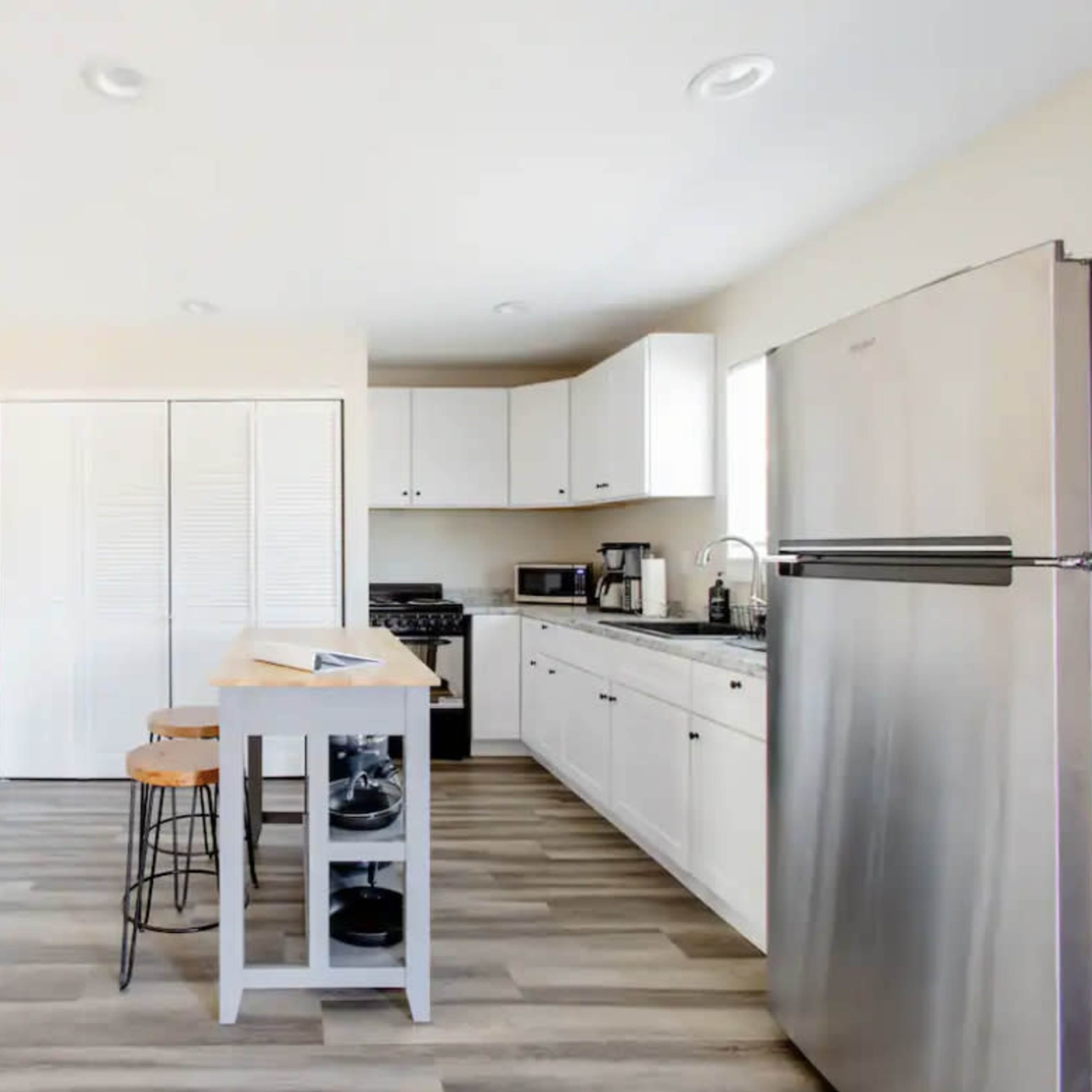 A modern kitchen with white cabinets, stainless steel appliances, and a small island with two stools.