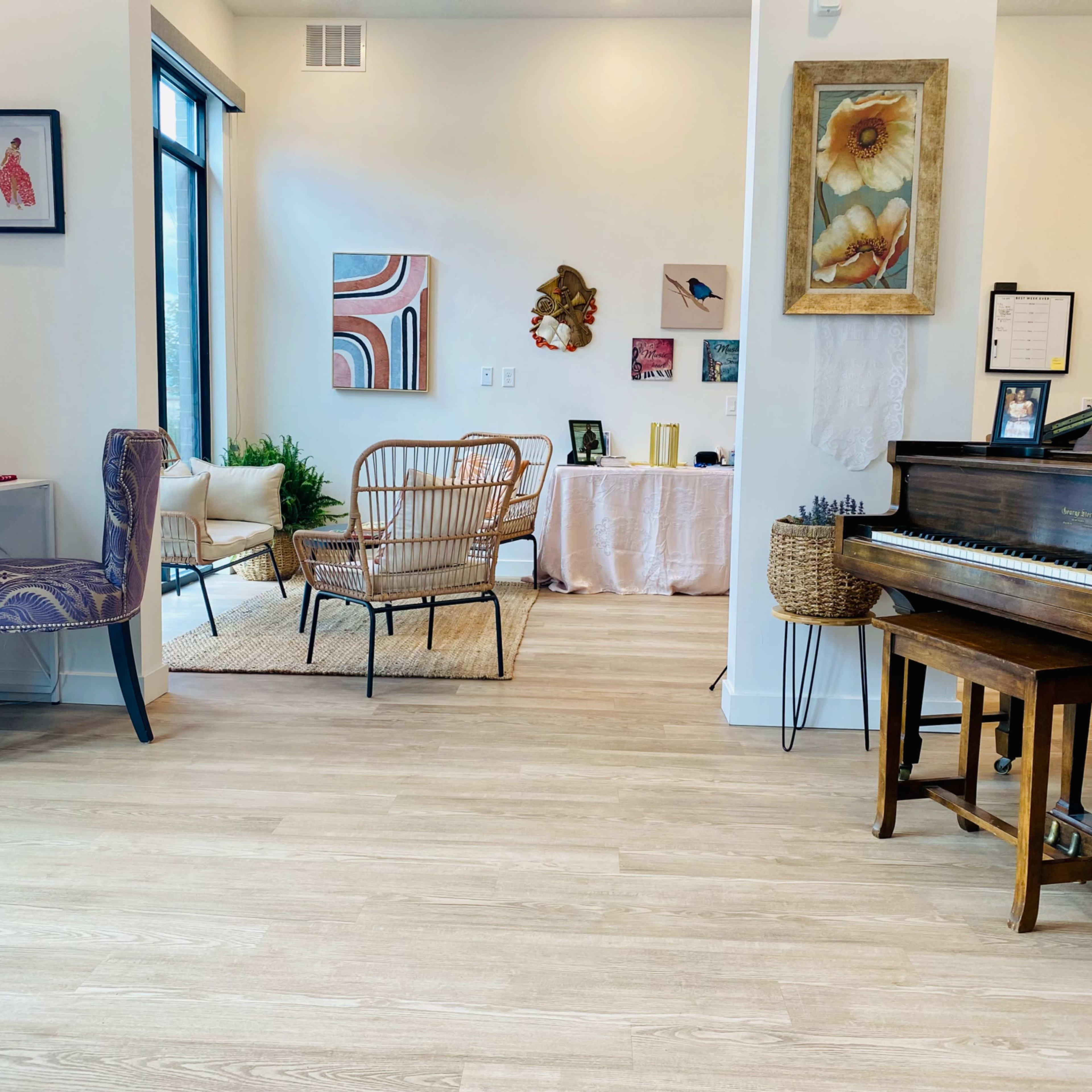 A bright, modern interior featuring a grand piano, a small desk with a chair, and a seating area with various artworks on the walls.