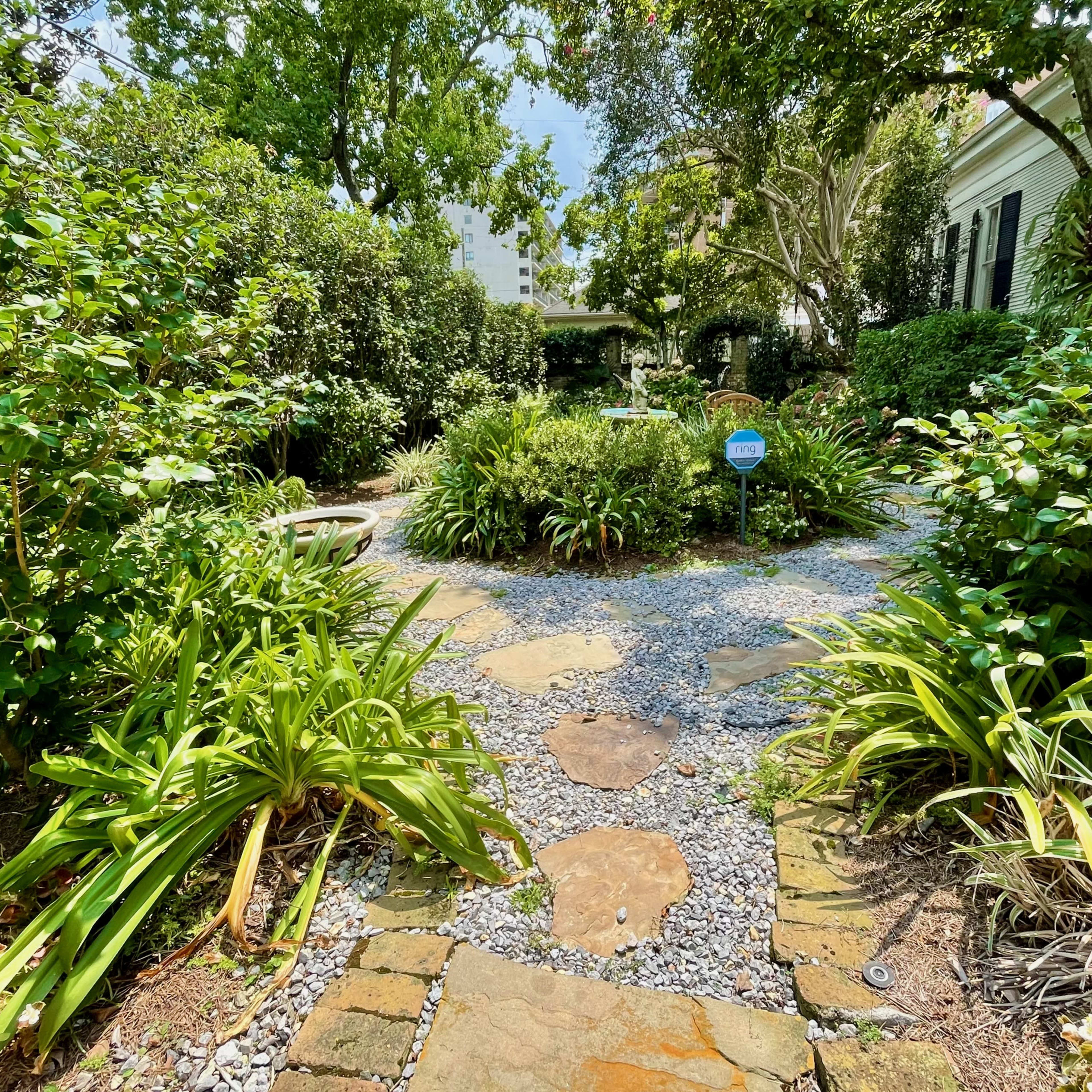 A stone pathway winds through a lush garden filled with greenery and shrubs.
