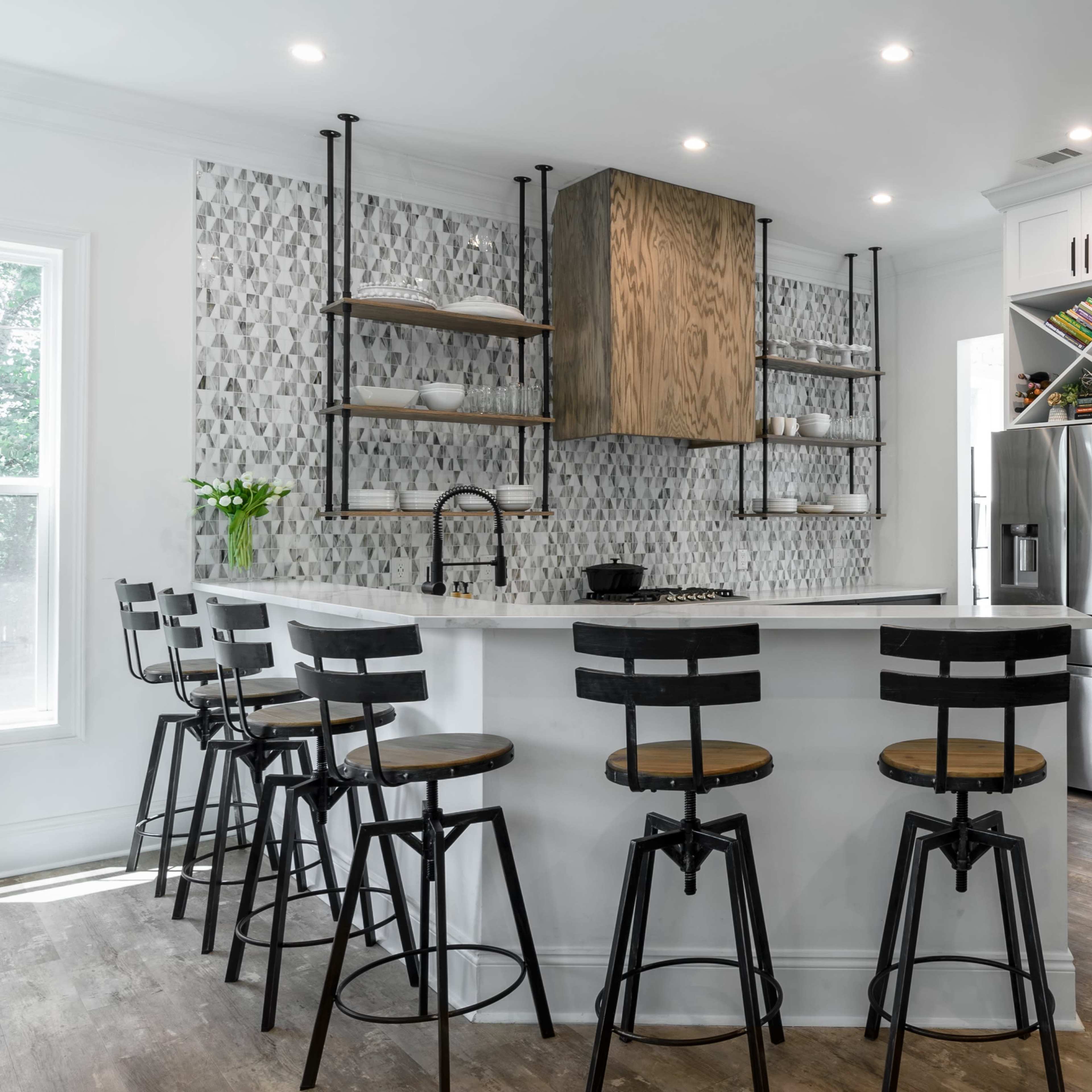 A modern kitchen features a central island with bar stools, sleek cabinetry, and tiled backsplash.